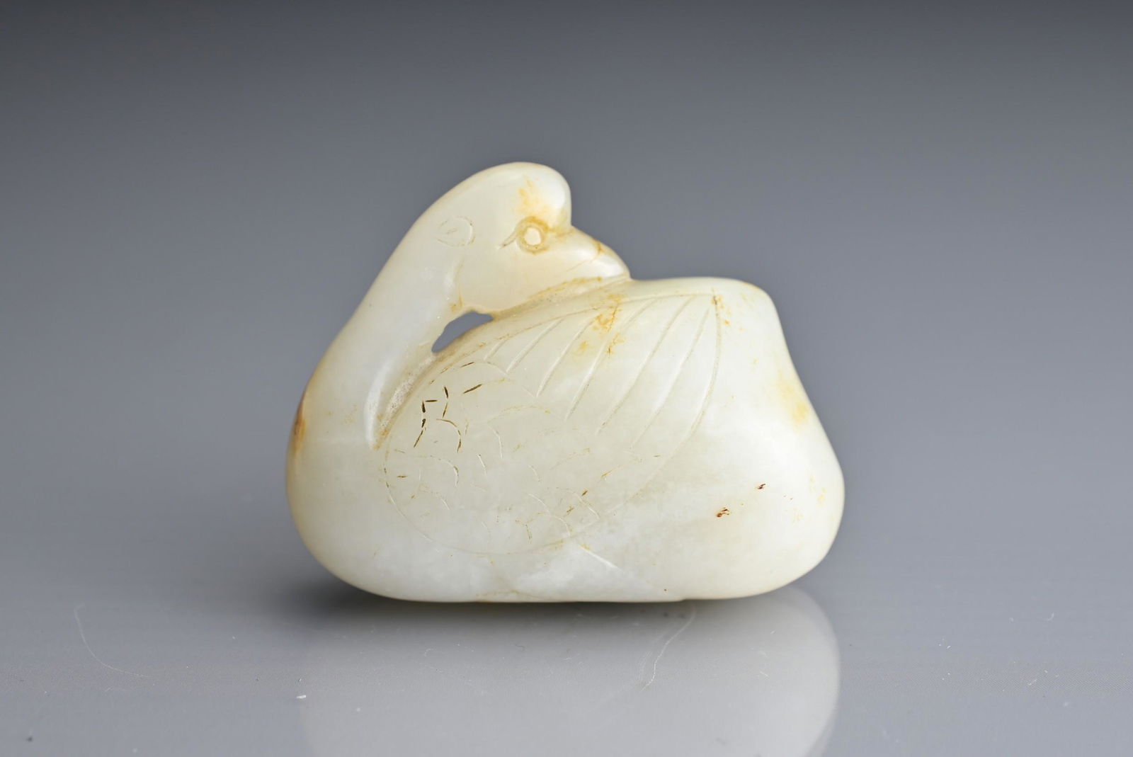 A CHINESE WHITE AND RUSSET JADE CARVING OF A CRANE, QING DYNASTY. Seated with its head turned to its (1 of 5)