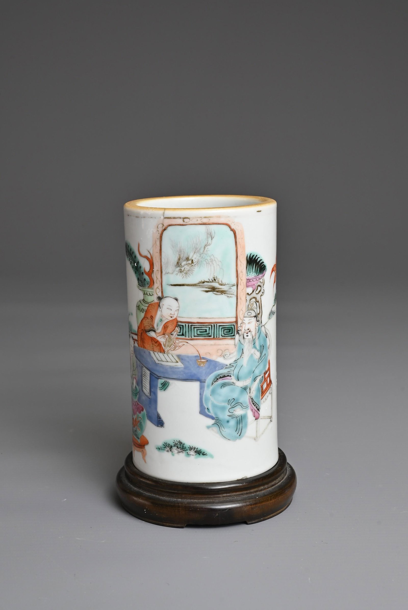 A CHINESE FAMILLE ROSE PORCELAIN BRUSH POT, BITONG, TONGZHI PERIOD. Of cylindrical form decorated: A CHINESE FAMILLE ROSE PORCELAIN BRUSH POT, BITONG, TONGZHI PERIOD. Of cylindrical form decorated with figure seated in a garden scene being served tea. Six-character seal mark of Tongzhi to base and 