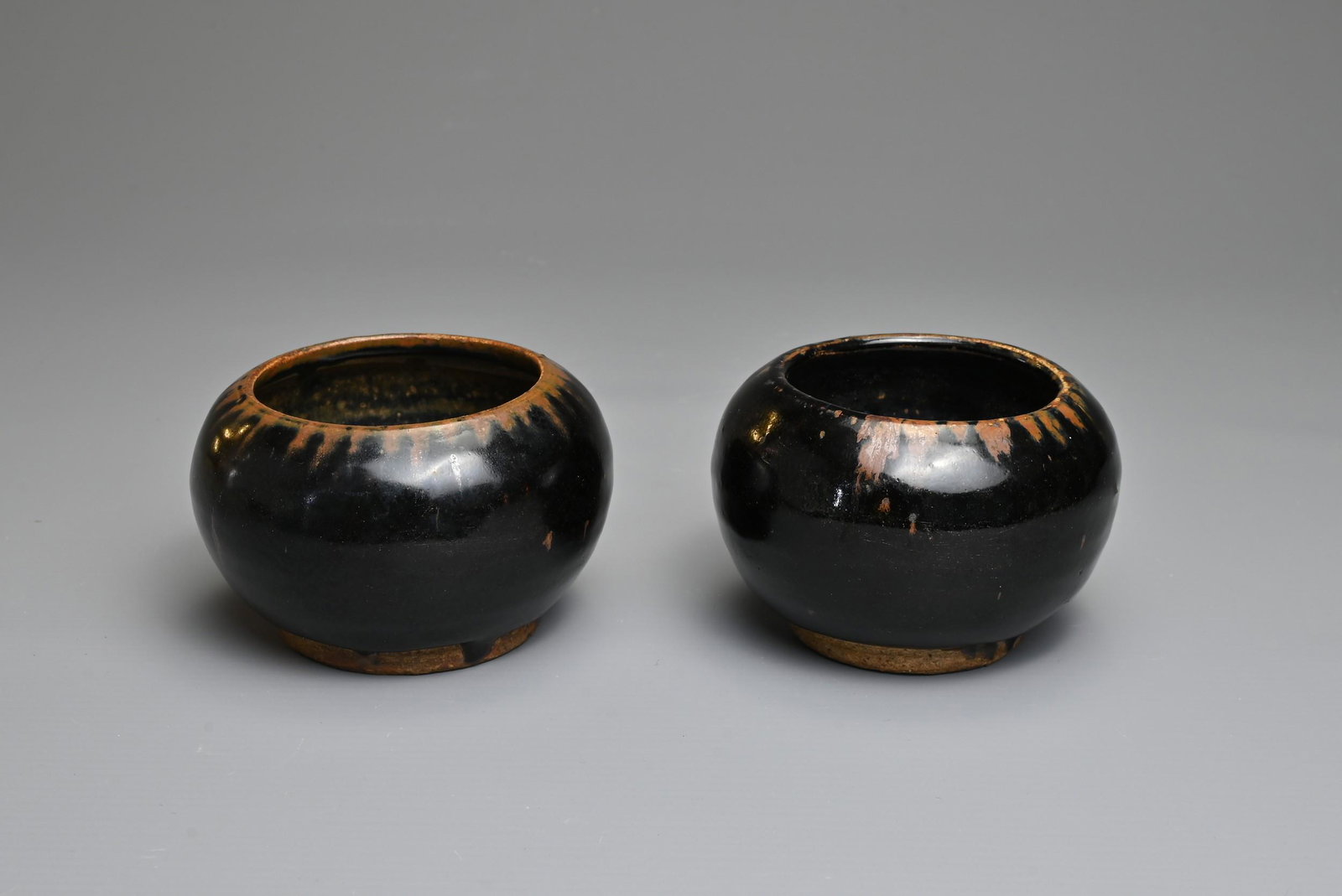TWO CHINESE HENAN BLACK GLAZED POTTERY JARS. Of globular form on a short foot with slightly concave (1 of 7)