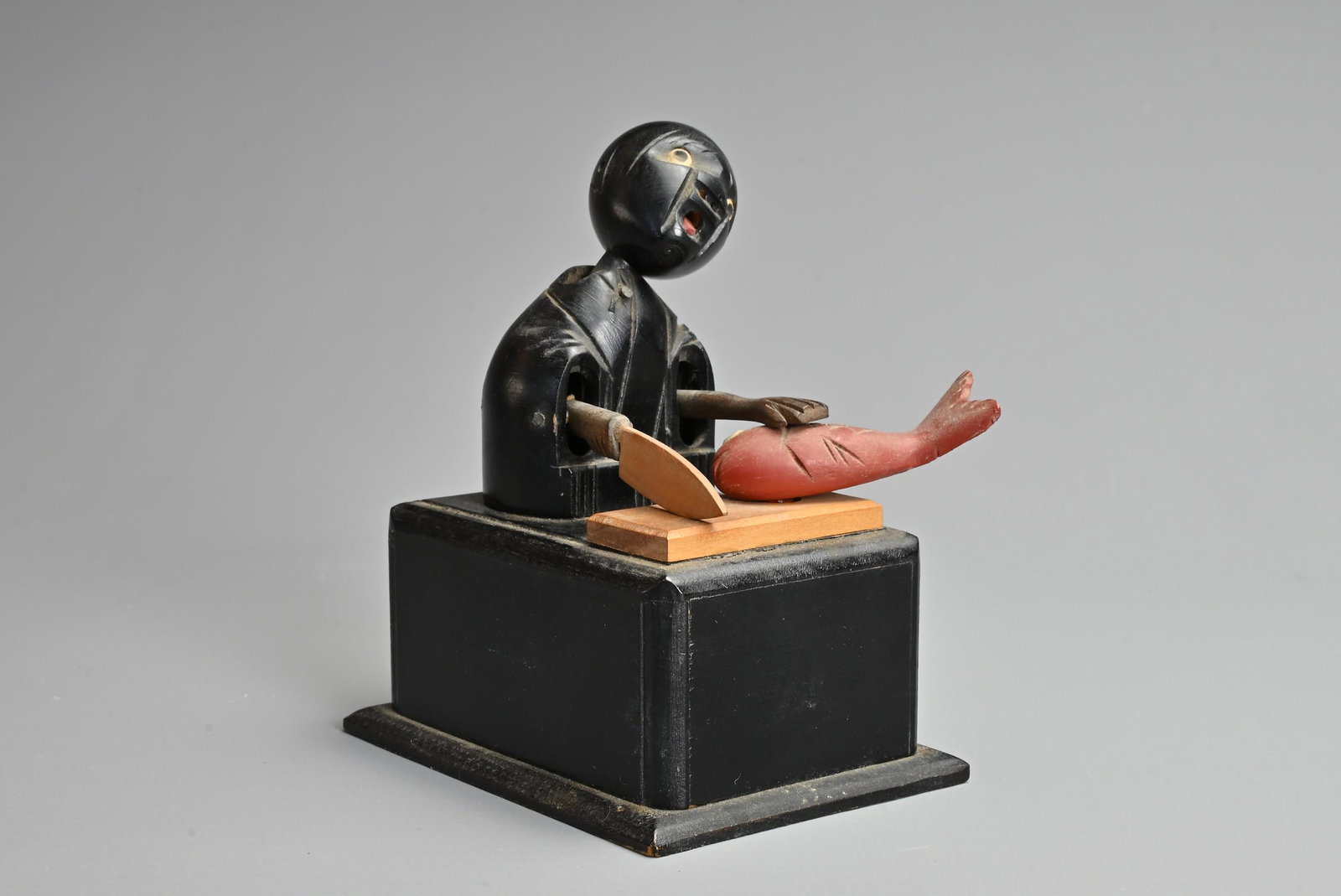 A JAPANESE WOOD KOBE TOY, 19/20TH CENTURY. An articulated modelled figure chopping fish. The figures: A JAPANESE WOOD KOBE TOY, 19/20TH CENTURY. An articulated modelled figure chopping fish. The figures head, arms and fish move when the handle is turned back and forth. 10.5cm tall.