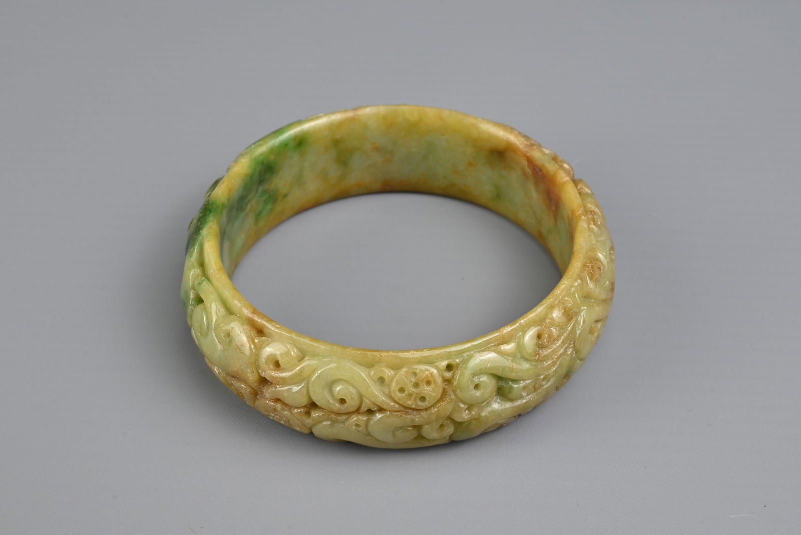 A CARVED CHINESE JADE BANGLE. Carved in relief with bat and lingzhi spray. The jade with yellow, (1 of 6)