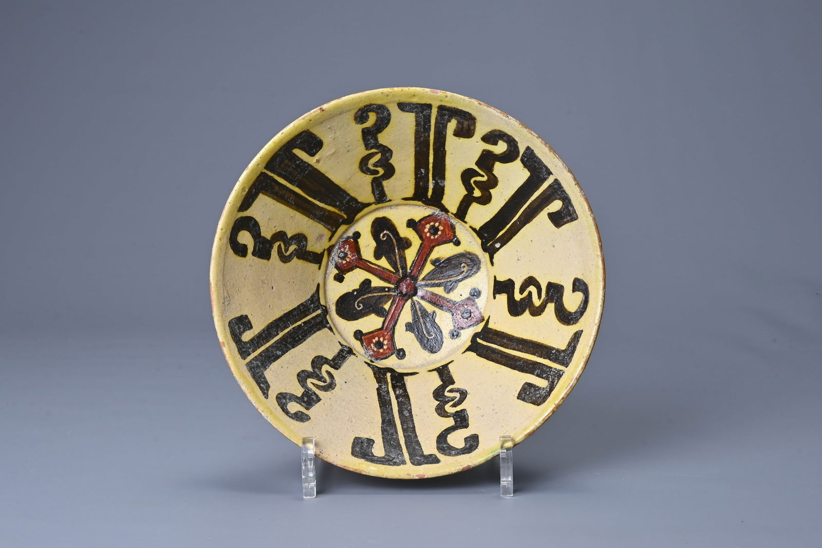 AN ISLAMIC POTTERY BOWL WITH KUFIC INSCRIPTION. Buff pottery bowl decorated with Kufic script in: AN ISLAMIC POTTERY BOWL WITH KUFIC INSCRIPTION. Buff pottery bowl decorated with Kufic script in brown slip on a white slip with further red motif. 20.3cm diam. Minor glaze chips to rim. No major sign