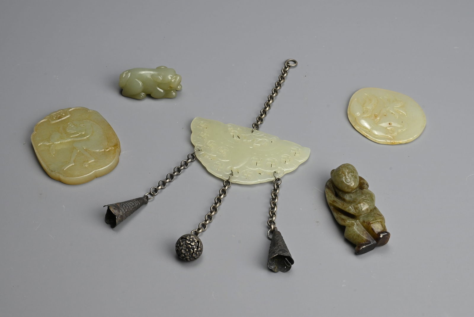 A GROUP OF CHINESE CELADON JADE ITEMS. To include a carved and pierced butterfly pendant with: A GROUP OF CHINESE CELADON JADE ITEMS. To include a carved and pierced butterfly pendant with Buddhist swastika decoration mounted with white metal pendants; Two pendants decorated in relief with figu