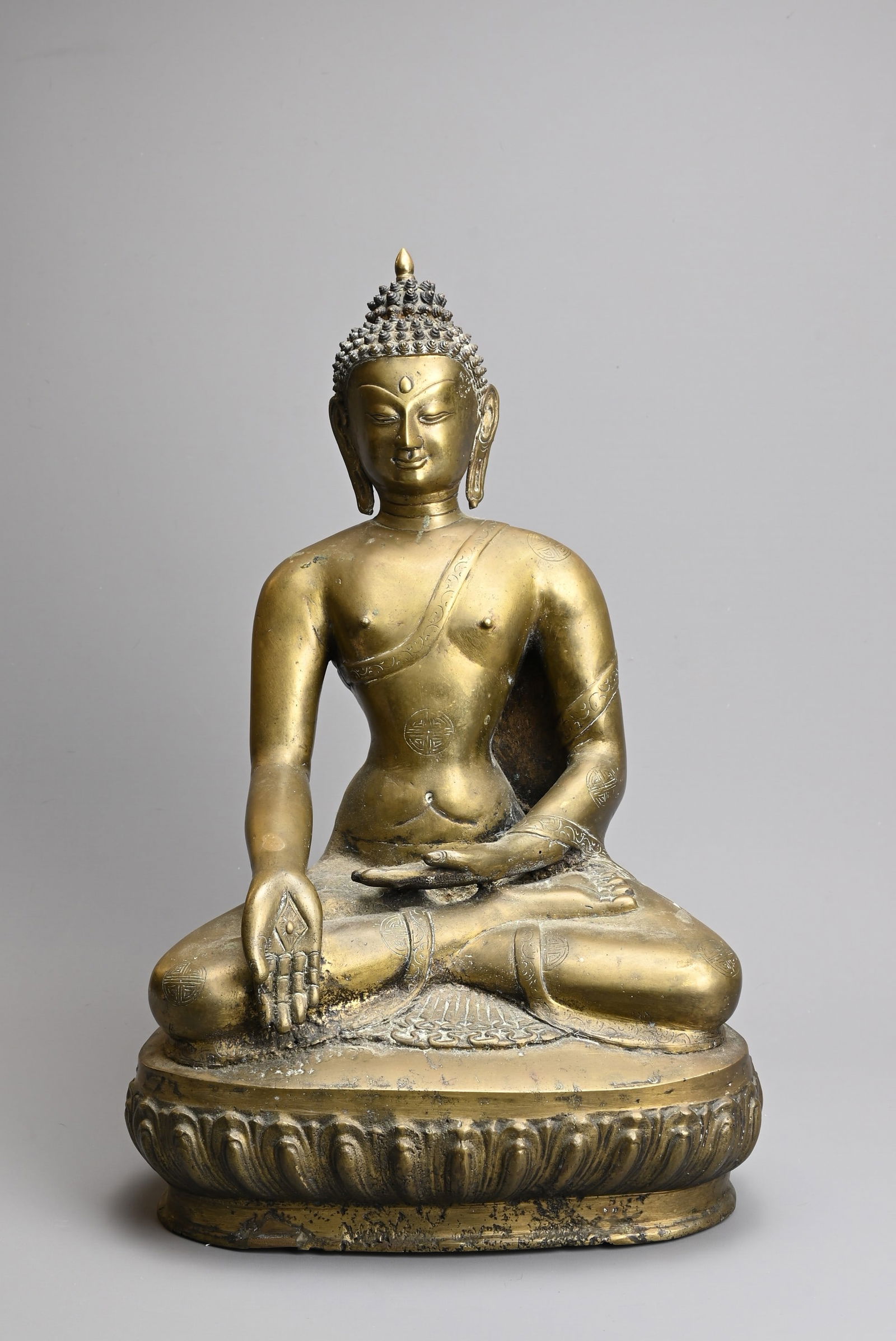 A TIBETAN CAST BRONZE FIGURE OF SHAKYAMUNI, 20TH CENTURY. Seated on a lotus base dressed in robes: A TIBETAN CAST BRONZE FIGURE OF SHAKYAMUNI, 20TH CENTURY. Seated on a lotus base dressed in robes decorated with Shou medallions. 39cm tall. The ushnisha separate from the head.