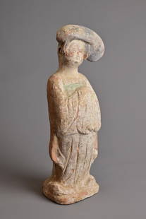 A CHINESE PAINTED POTTERY FIGURE OF COURT LADY, TANG DYNASTY (AD 618-907). Modelled standing wearing: A CHINESE PAINTED POTTERY FIGURE OF COURT LADY, TANG DYNASTY (AD 618-907). Modelled standing wearing a long flowing robe, her coiffured hair worn high to one side and her features picked out in black,