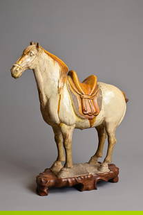 A CHINESE SANCAI GLAZED POTTERY MODEL OF A HORSE, TANG DYNASTY (AD 618-907). Modelled standing: A CHINESE SANCAI GLAZED POTTERY MODEL OF A HORSE, TANG DYNASTY (AD 618-907). Modelled standing foursquare, with an amber glazed mane, saddle and tail, the horse's body in cream glaze, on a rectangular