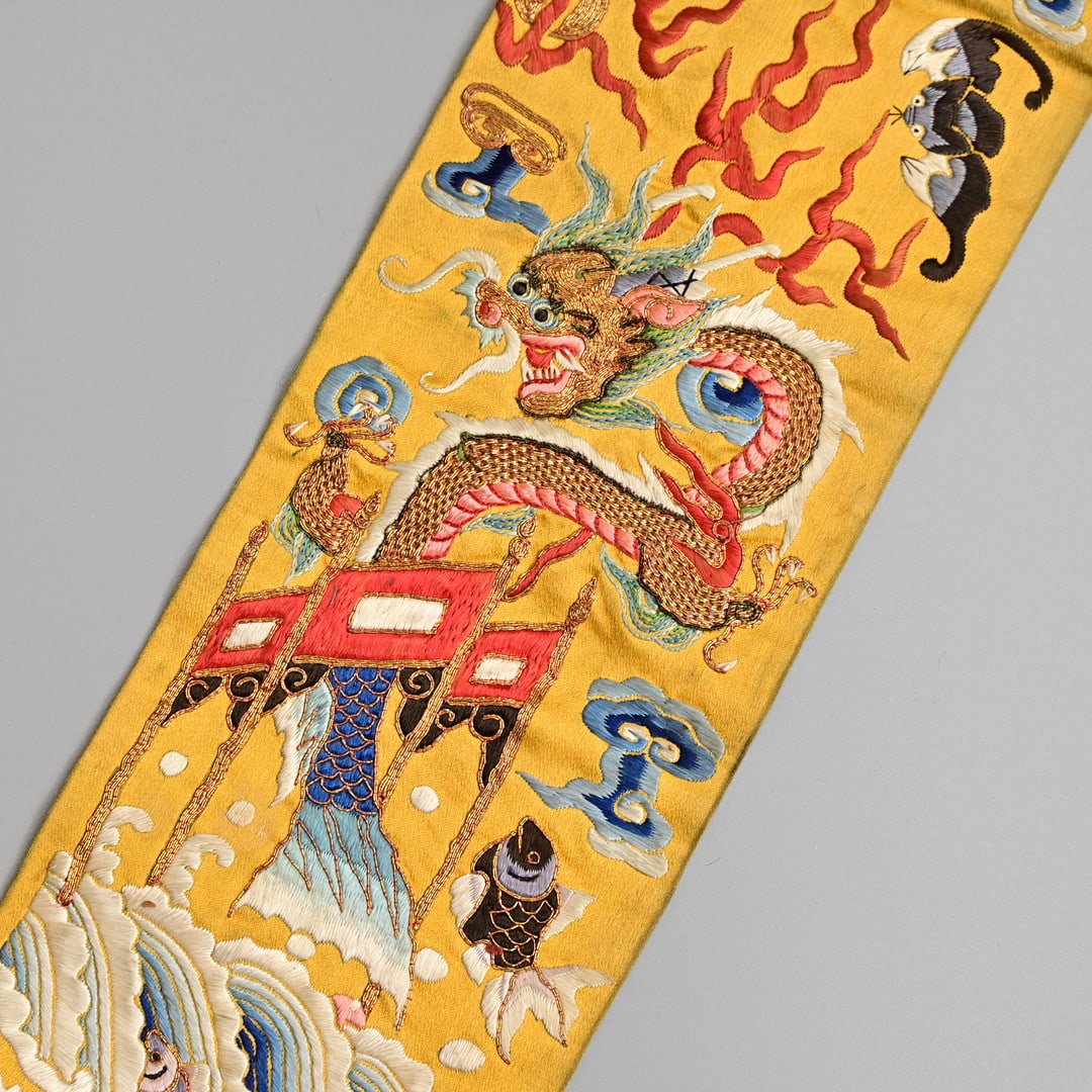 A CHINESE GOLD GROUND EMBROIDERED SILK SLEEVE CUFF, QING DYNASTY.: Embroidered in gold and coloured silk threads, depicting a carp transforming into a dragon, before butterflies, bats, flowers and birds, 10 cm wide x 113cm long.