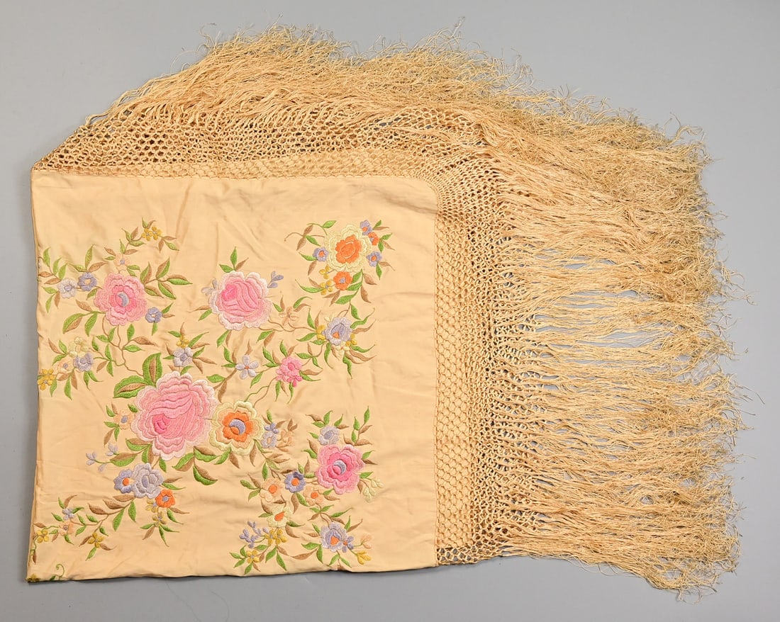 A CHINESE PALE APRICOT COLOURED EMBROIDERED SILK SHAWL, EARLY 20TH CENTURY.: Embroidered with loose flower-sprays, with long tasselled fringed border, 130cm square exc. tassels.