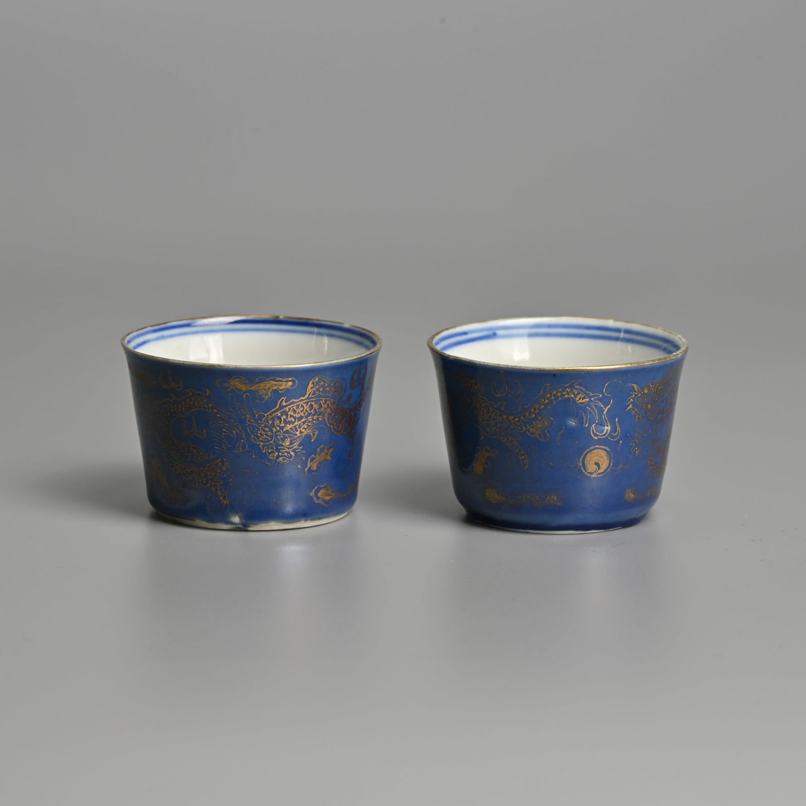 A PAIR OF CHINESE BLUE-GROUND AND GILT DECORATED 'DRAGON' PORCELAIN CUPS, QING DYNASTY.: A PAIR OF CHINESE BLUE-GROUND AND GILT DECORATED 'DRAGON' PORCELAIN CUPS, QING DYNASTY. Decorated in gilt with dragons chasing flaming pearls. Each with six-character marks of Guangxu to base in under
