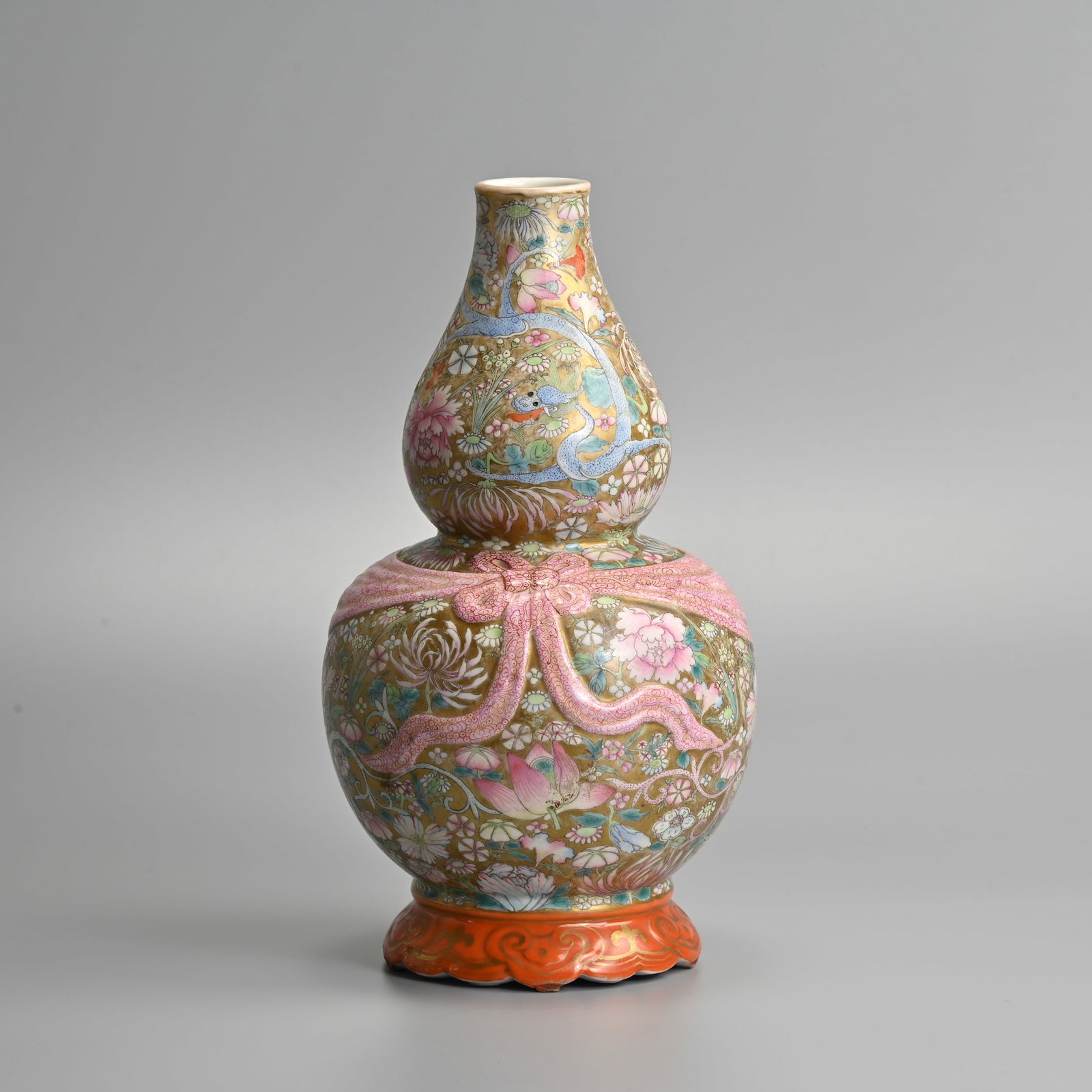 A CHINESE FAMILLE ROSE RIBBONED DOUBLE GOURD PORCELAIN VASE, REPUBLIC PERIOD.: A CHINESE FAMILLE ROSE RIBBONED DOUBLE GOURD PORCELAIN VASE, REPUBLIC PERIOD. Decorated with various flowers and chilong reserved on a gilt ground. The waist tied with a ruby enamelled sash deco
