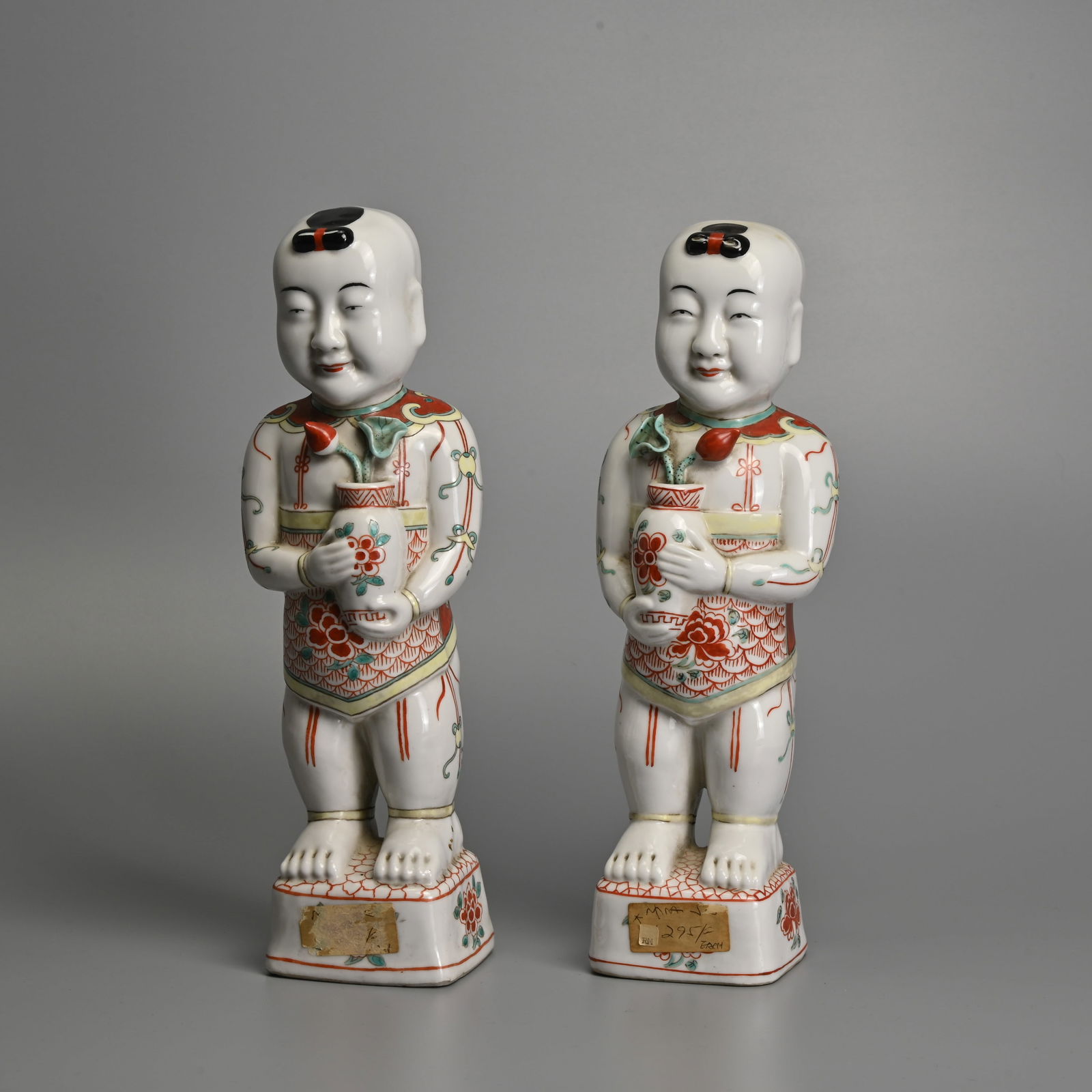 A MIRRORED PAIR OF CHINESE FAMILLE VERTE PORCELAIN MODELS OF BOYS, 19TH CENTURY.: A MIRRORED PAIR OF CHINESE FAMILLE VERTE PORCELAIN MODELS OF BOYS, 19TH CENTURY. Both standing atop a square form base decorated with peony heads, wearing a dudou and holding a vase with a lotus spray