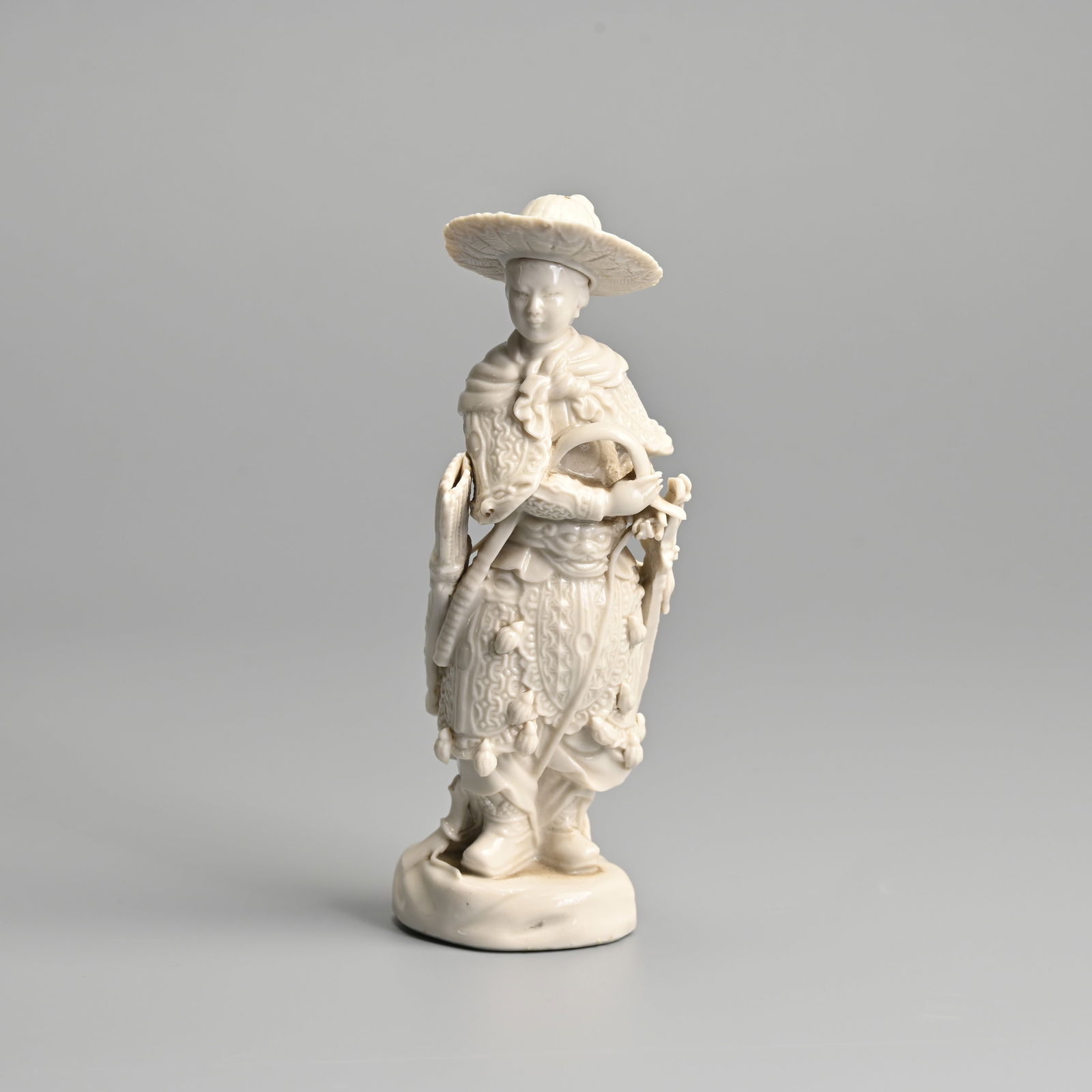 A CHINESE DEHUA PORCELAIN FIGURE OF AN ARCHER, QING / REPUBLIC PERIOD.: A CHINESE DEHUA PORCELAIN FIGURE OF AN ARCHER, QING / REPUBLIC PERIOD. Well modelled, standing on a rockwork base dressed in armour with a brimmed hat holding a bow, with quiver and sword hanging at t