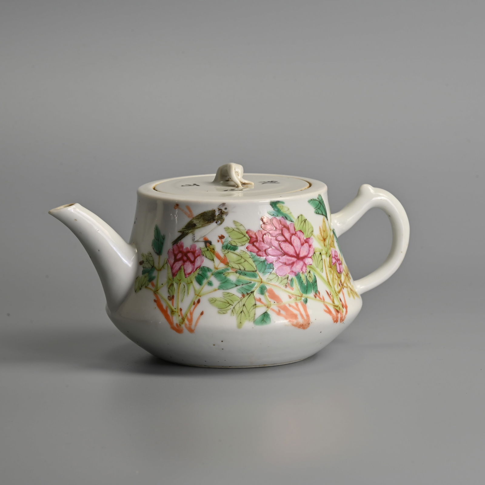 A CHINESE PORCELAIN FAMILLE ROSE TEAPOT AND COVER, MID-20TH CENTURY.: A CHINESE PORCELAIN FAMILLE ROSE TEAPOT AND COVER, MID-20TH CENTURY. Painted with a bird perched amongst pink flowers and green leaves, inscribed in black calligraphic script, 18 cm wide. Condition: M