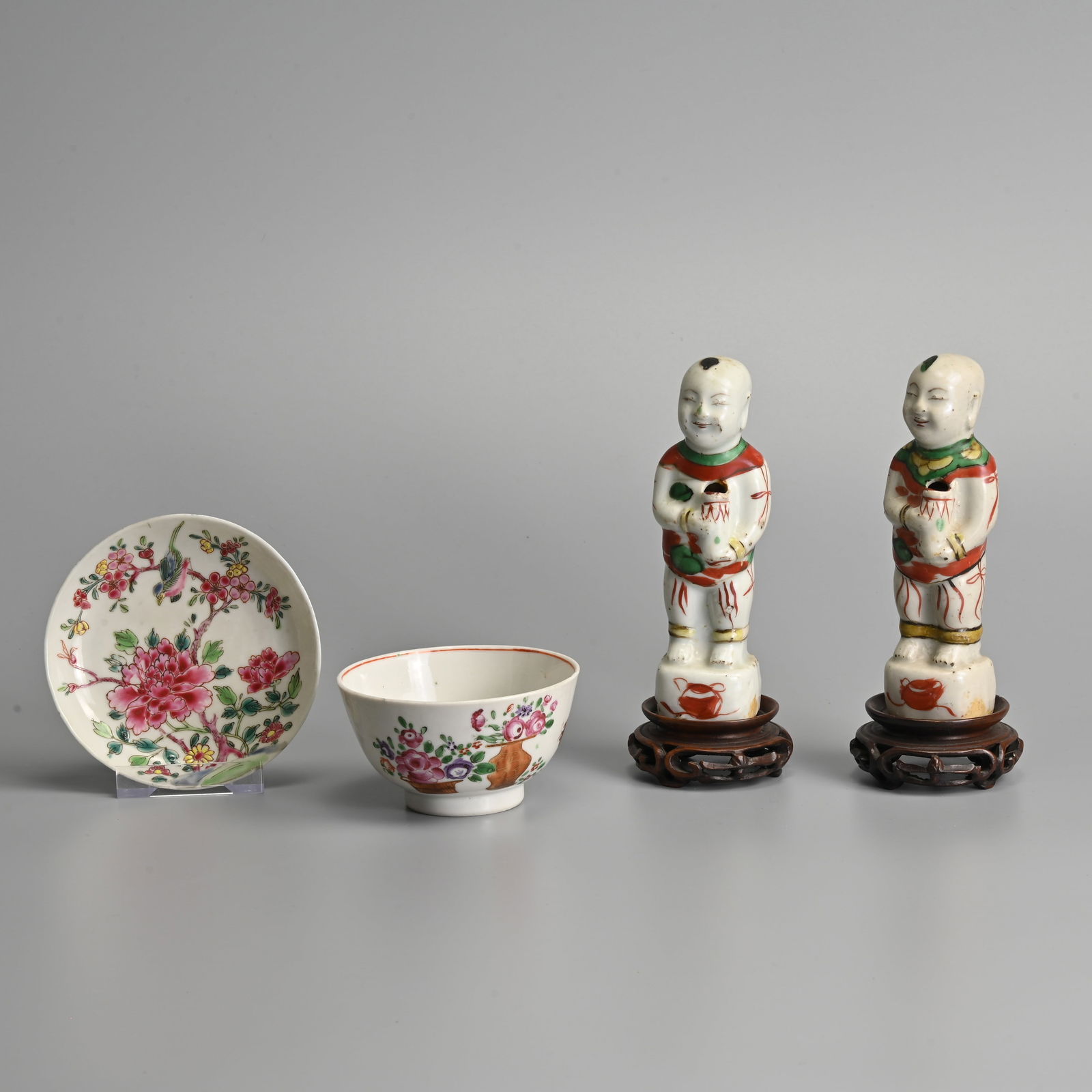 A CHINESE EXPORT FAMILLE ROSE SAUCER, A TEA BOWL AND A PAIR OF FAMILLE VERTE MODELS OF HO-HO BOYS, 1: A CHINESE EXPORT FAMILLE ROSE SAUCER, A TEA BOWL AND A PAIR OF FAMILLE VERTE MODELS OF HO-HO BOYS, 18TH CENTURY AND LATER. The saucer, early 18th century, painted with a bird perched amongst flowering