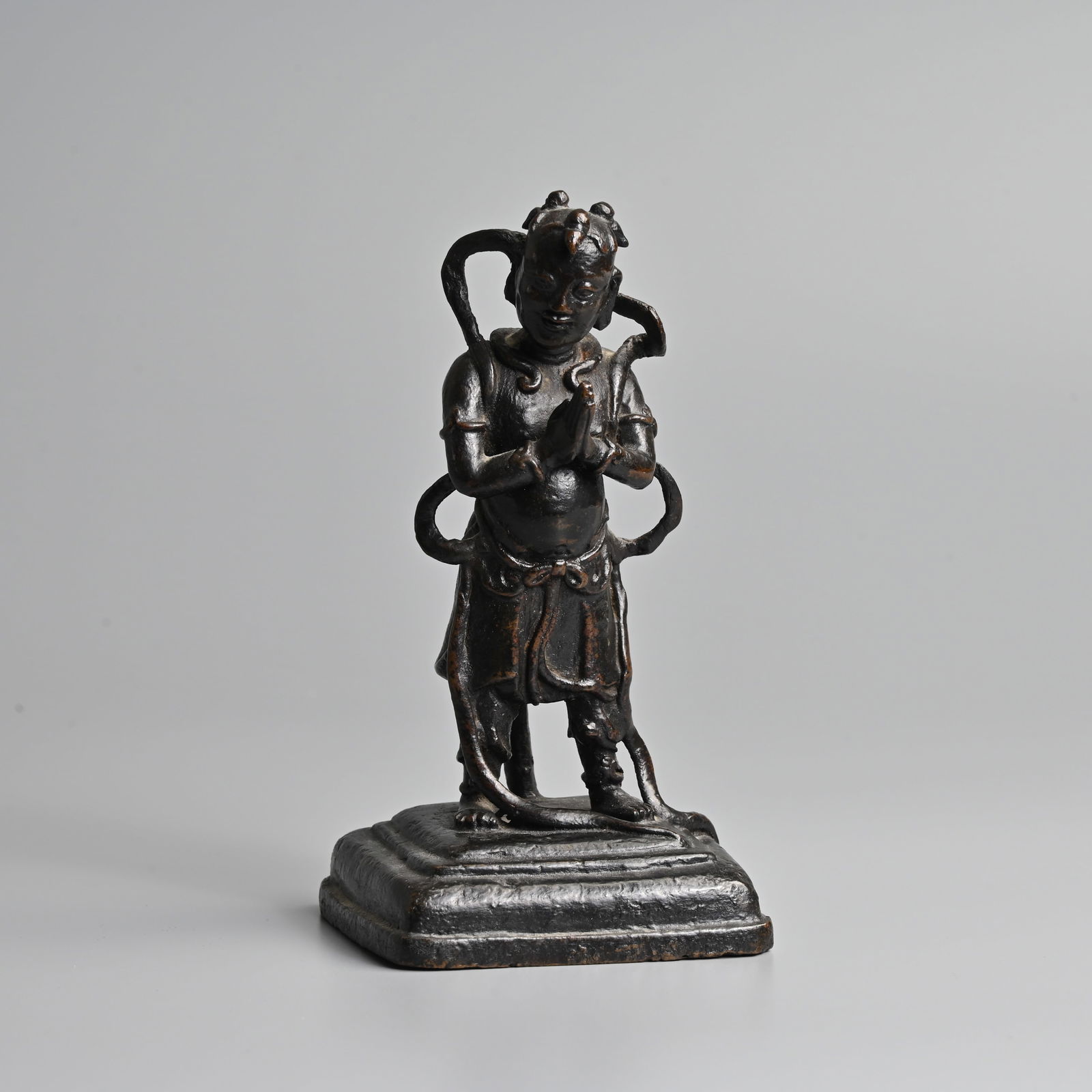 A CHINESE BRONZE FIGURE OF A BOY, 17/18TH CENTURY.: A CHINESE BRONZE FIGURE OF A BOY, 17/18TH CENTURY. Well cast figure standing on a square form base with his hands clasped before his chest in adoration. 15.5cm tall. Weight 570 grams. Condition: In go