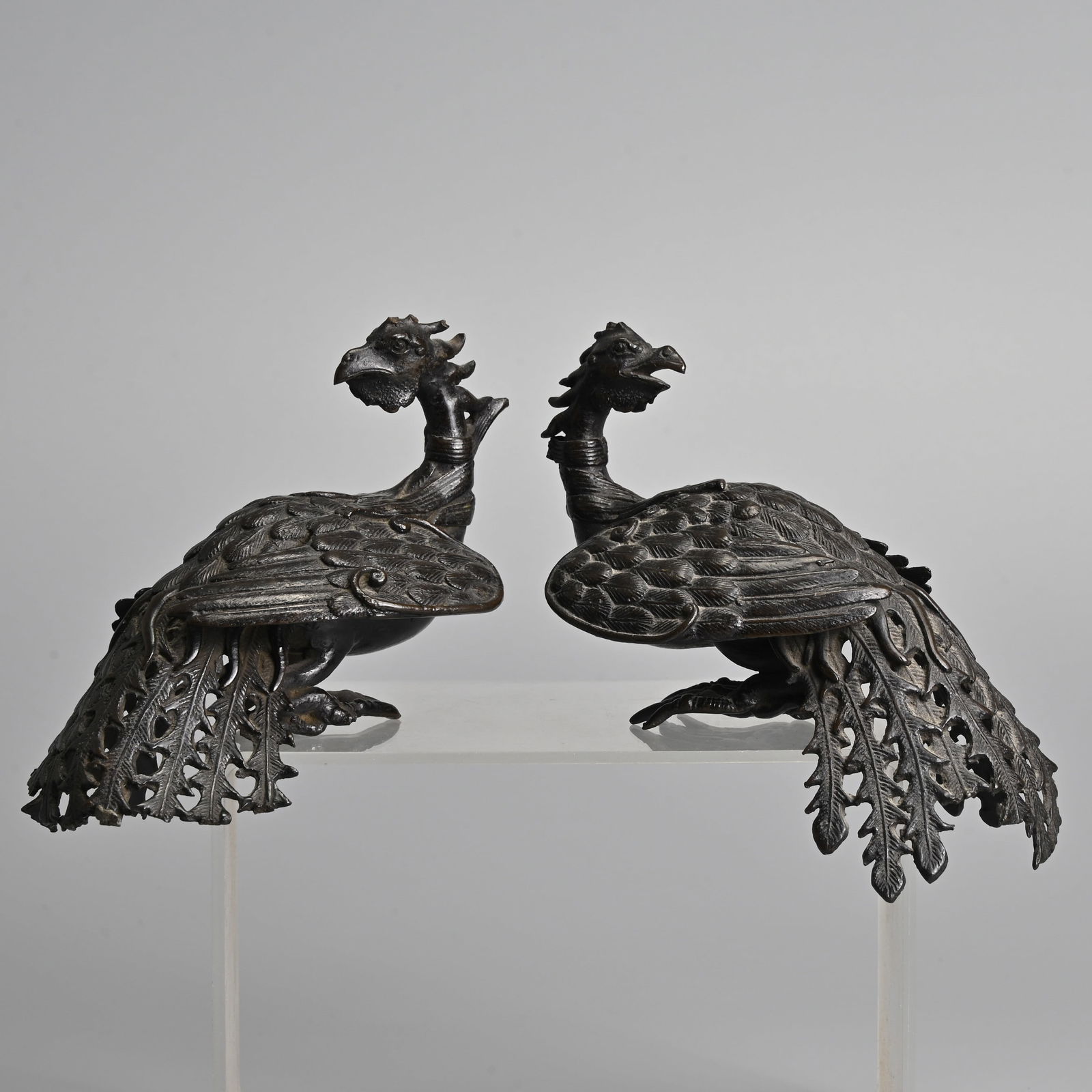 A PAIR OF CHINESE FINELY CAST BRONZE MODELS OF PHOENIX, 17/18TH CENTURY.: A PAIR OF CHINESE FINELY CAST BRONZE MODELS OF PHOENIX, 17/18TH CENTURY. Seated with their feet tucked under their bodies with their wings folded and their heads turned backwards. 15cm length. (2) The