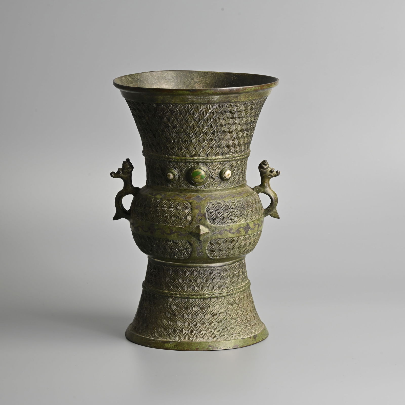 A CHINESE ARCHAISTIC BRONZE VESSEL, QING / REPUBLIC PERIOD.: A CHINESE ARCHAISTIC BRONZE VESSEL, QING / REPUBLIC PERIOD. Of gu form with twin animal form handles decorated to the body with continuous hexagonal and rope twist bands with circular stone inserts. 2