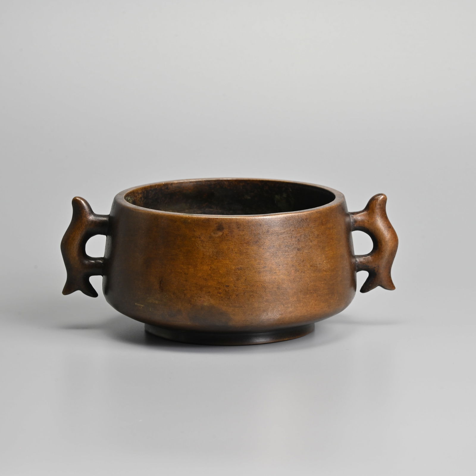 A CHINESE BRONZE TWIN FISH HANDLED CENSER, 20TH CENTURY.: A CHINESE BRONZE TWIN FISH HANDLED CENSER, 20TH CENTURY. Compressed body tapered to the rim with two fish form handles, raised on a short foot. Four-character mark to base in relief. 19.5cm wide inclu