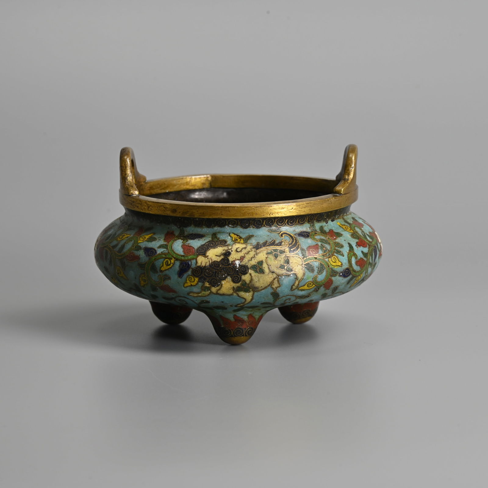 A CHINESE CLOISONNE ENAMEL TRIPOD CENSER, 18/19TH CENTURY.: A CHINESE CLOISONNE ENAMEL TRIPOD CENSER, 18/19TH CENTURY. With two looped handles, decorated in coloured enamels with Dogs of Fo and lotus flowers on leafy stems on a turquoise ground. The base with