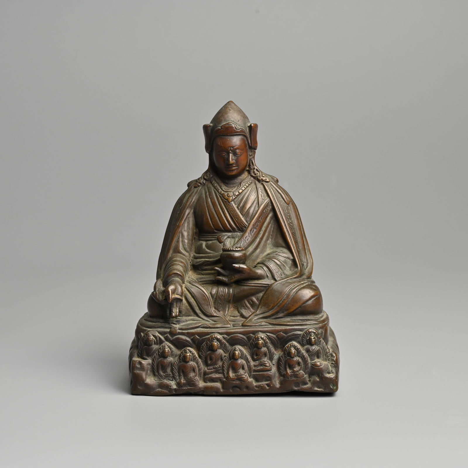 A SINO TIBETAN BRONZE FIGURE OF PADMASAMBHAVA, QING DYNASTY.: A SINO TIBETAN BRONZE FIGURE OF PADMASAMBHAVA, QING DYNASTY. The medicine Buddha seated on a lotus base holding a bowl and myrobalan fruit with eight further Buddhas. With impressed inscription to ver