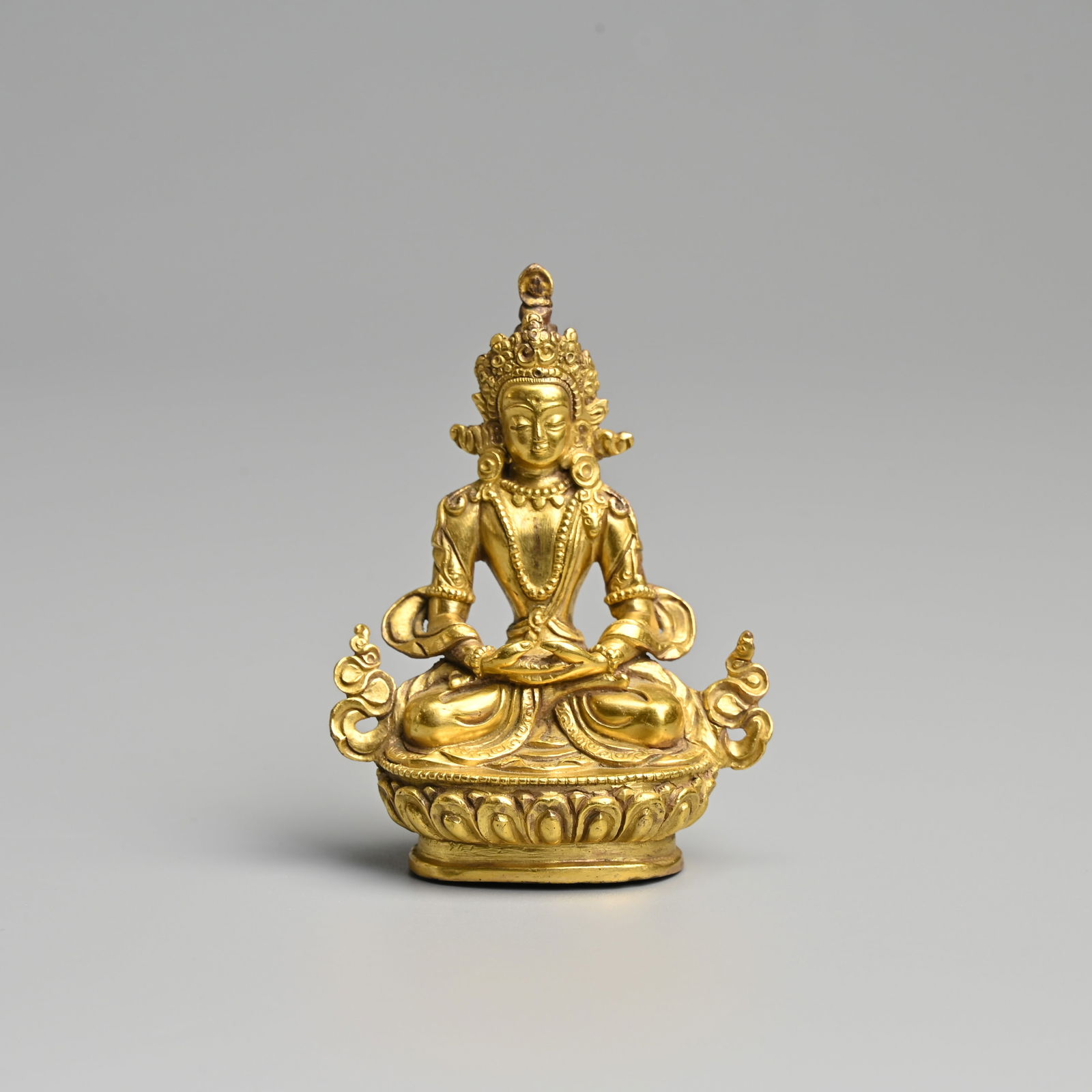 A SMALL SINO TIBETAN GILT BRONZE FIGURE OF AMITAYUS.: A SMALL SINO TIBETAN GILT BRONZE FIGURE OF AMITAYUS. Seated on a lotus base dressed in robes with jewelled necklace and crown. 8cm tall. Weight 158 grams. Condition: In good overall condition with no