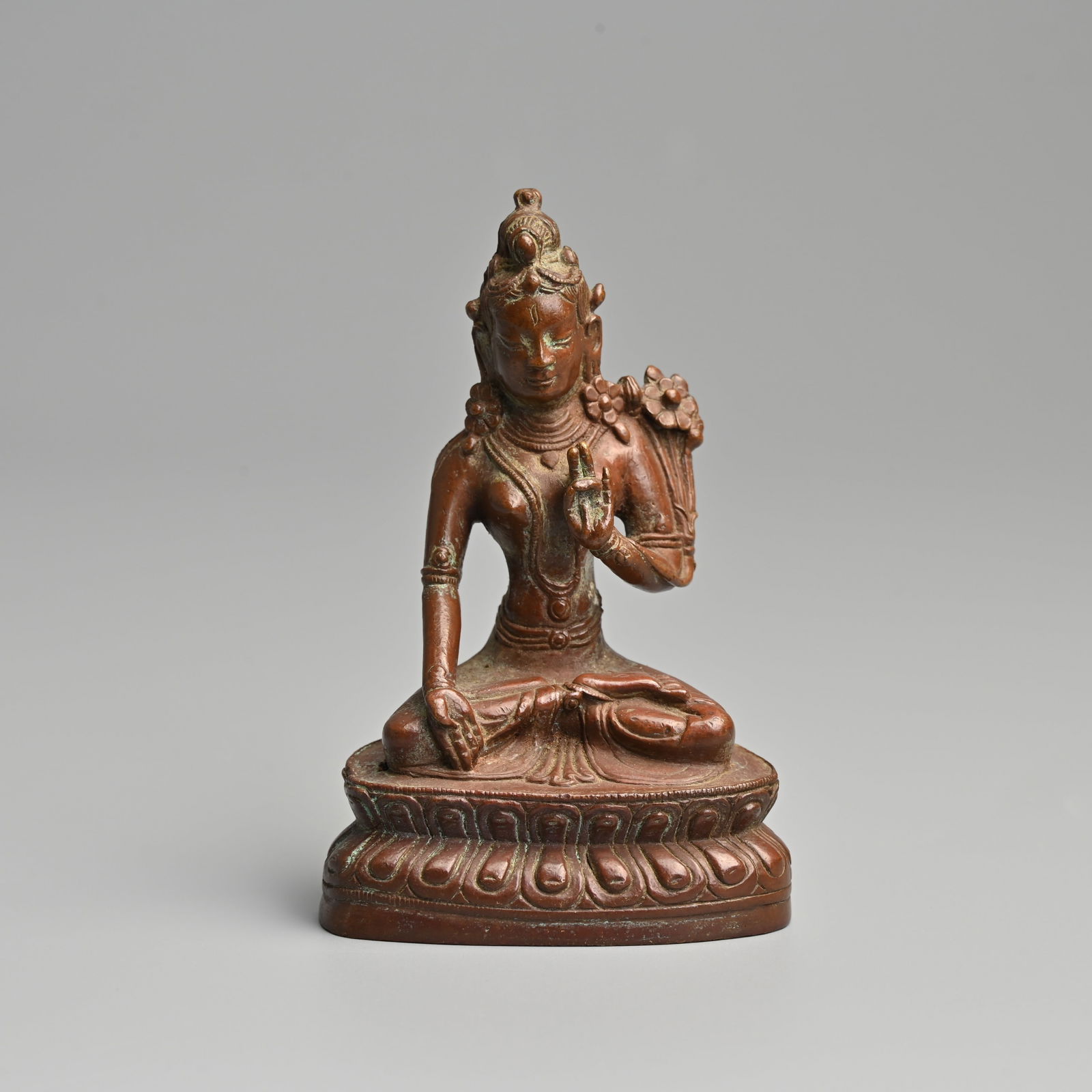 A SMALL NEPALESE BRONZE FIGURE OF SEATED TARA, 19TH CENTURY.: A SMALL NEPALESE BRONZE FIGURE OF SEATED TARA, 19TH CENTURY. Heavily cast seated on a lotus base wearing robes and jewelled necklace with cuff bracelets and arm bands, holding a floral spray in her le