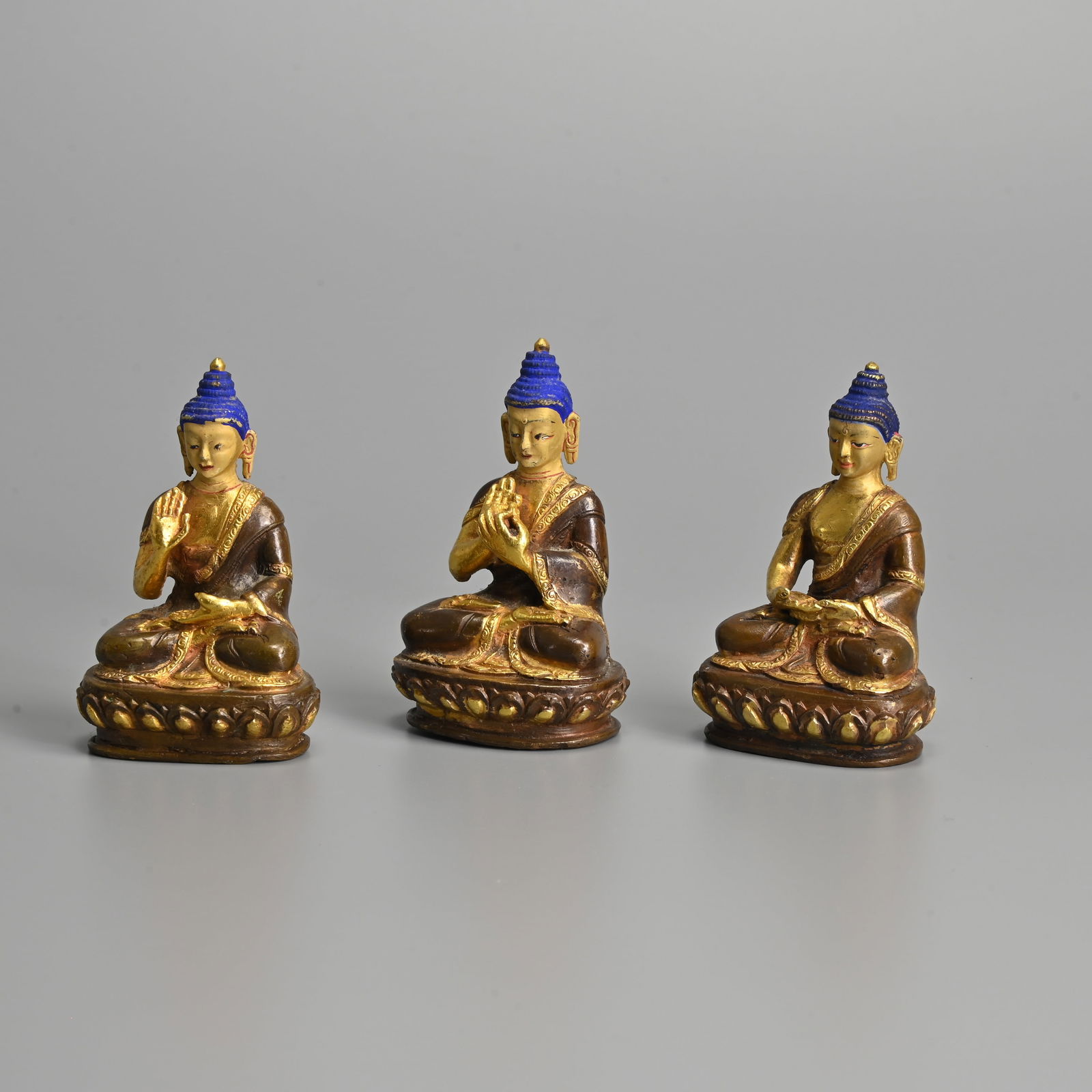 THREE SINO TIBETAN PARCEL GILT BRONZE FIGURES OF BUDDHA, 20TH CENTURY.: THREE SINO TIBETAN PARCEL GILT BRONZE FIGURES OF BUDDHA, 20TH CENTURY. Seated on lotus bases dress in robes depicted in various postures. Each with floral mark to base. 7.7cm tall (3). Condition: No d