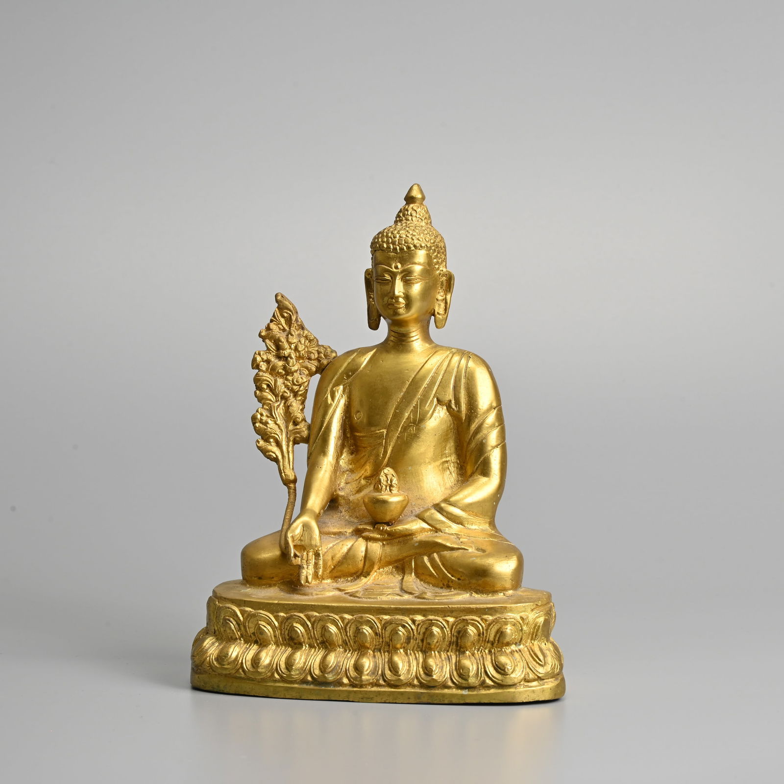 A SINO TIBETAN GILT BRONZE FIGURE OF BHAISAJYAGURU, 20TH CENTURY.: A SINO TIBETAN GILT BRONZE FIGURE OF BHAISAJYAGURU, 20TH CENTURY. The medicine Buddha seated in padmasana upon a double lotus throne with right hand held in varada mudra holding a Myrobalan plant stem