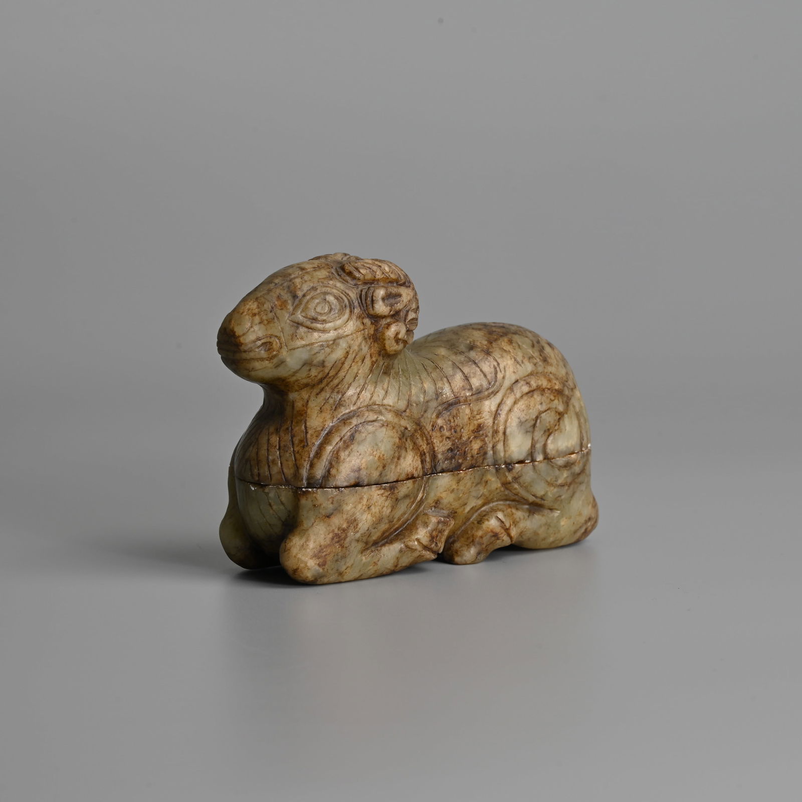 A CHINESE CARVED JADE BOX AND COVER IN THE FORM OF A RECUMBENT RAM, 20TH CENTURY.: A CHINESE CARVED JADE BOX AND COVER IN THE FORM OF A RECUMBENT RAM, 20TH CENTURY. The ram carved with its legs tucked under its body in the Han dynasty style. 10cm length. Condition: Small nibbles to