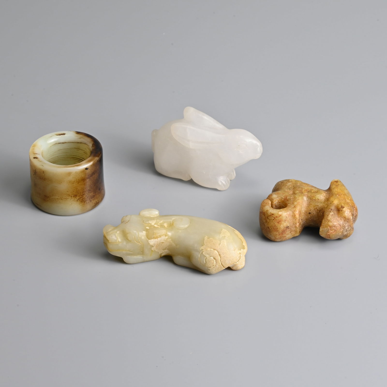 A GROUP OF CHINESE CARVED JADE ITEMS.: A GROUP OF CHINESE CARVED JADE ITEMS. To include a thumb ring incised with fish and inscription; A white jade carving of a rabbit; A pale celadon jade carving of a mythical beast; Together with a Neol
