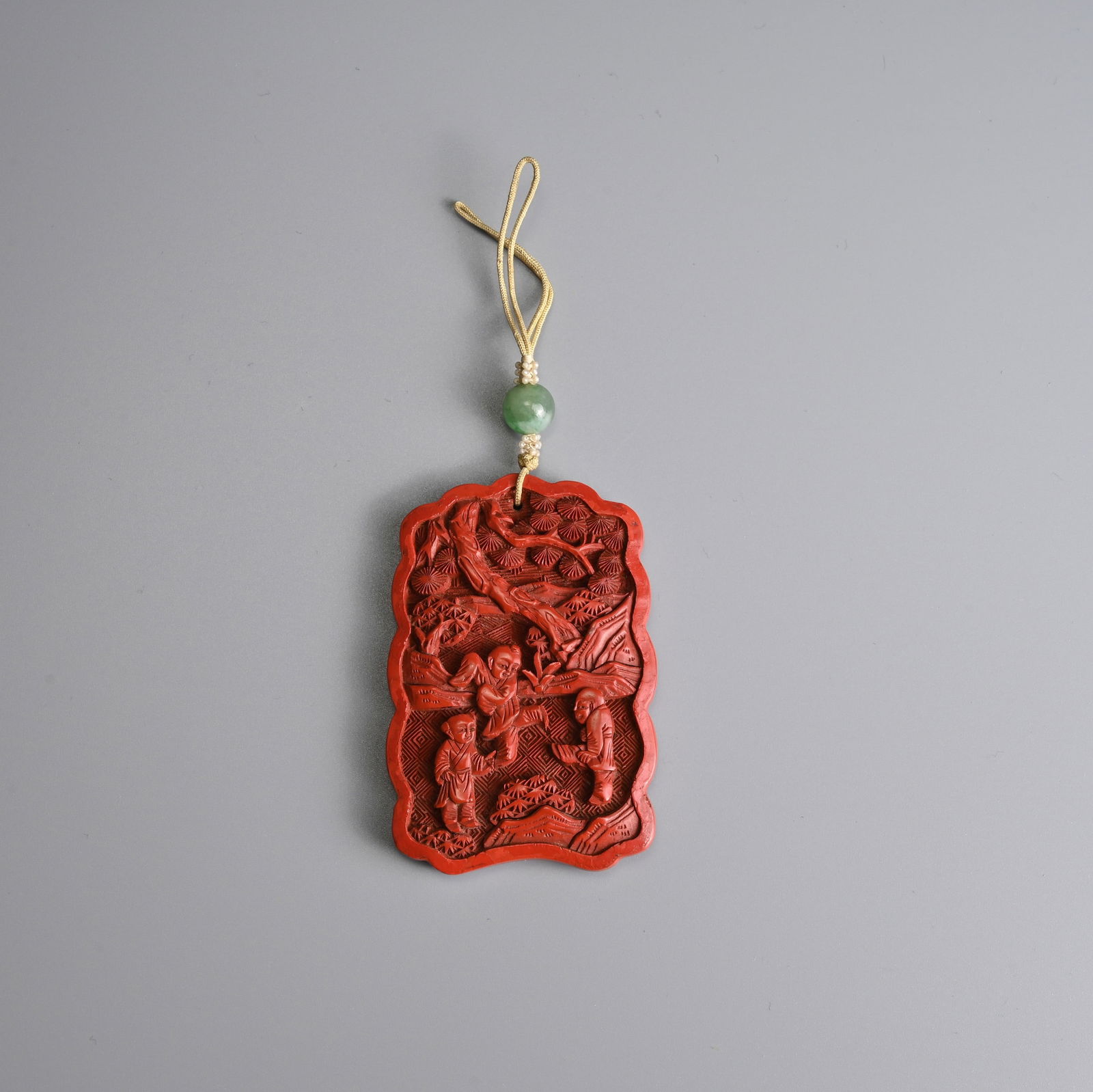 A CHINESE CINNABAR LACQUER 'BOYS' PENDANT, 19/20TH CENTURY.: A CHINESE CINNABAR LACQUER 'BOYS' PENDANT, 19/20TH CENTURY. Well carved to both sides in relief with scenes of boys at play in landscape with trees and rockwork. Strung on seed pearls and jade bead. P