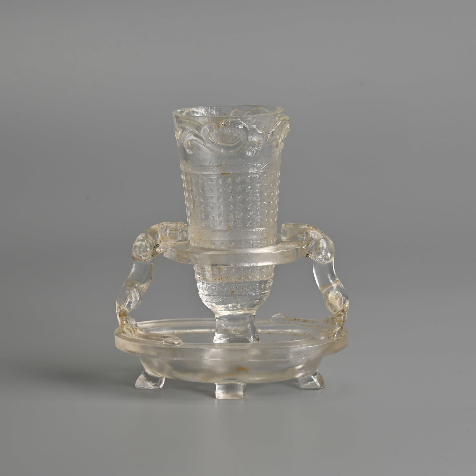 A CHINESE ROCK CRYSTAL CUP AND STAND, QING DYNASTY: A CHINESE ROCK CRYSTAL CUP AND STAND, QING DYNASTY The cup carved in relief with bands of scroll work with stylised chilong and phoenix to the rim. The open work base raised on four feet, supported by