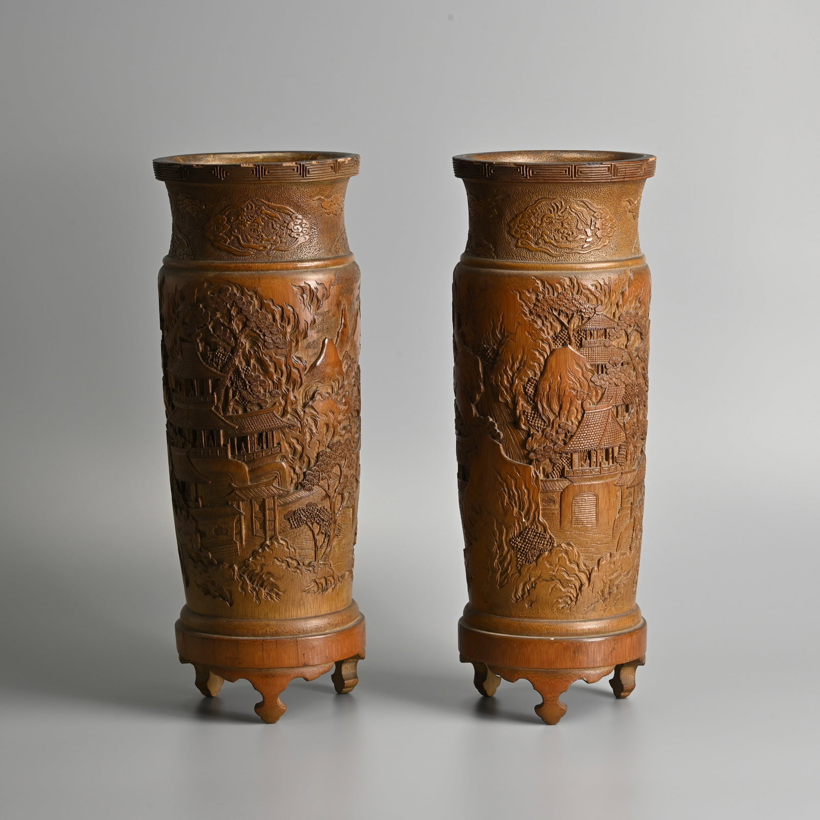 A LARGE PAIR OF CHINESE CARVED BAMBOO BRUSH POTS ON TRIPOD STANDS, QING DYNASTY.: A LARGE PAIR OF CHINESE CARVED BAMBOO BRUSH POTS ON TRIPOD STANDS, QING DYNASTY. Single sections of bamboo carved in relief featuring a continuous mountain landscape with buildings and trees, below cl
