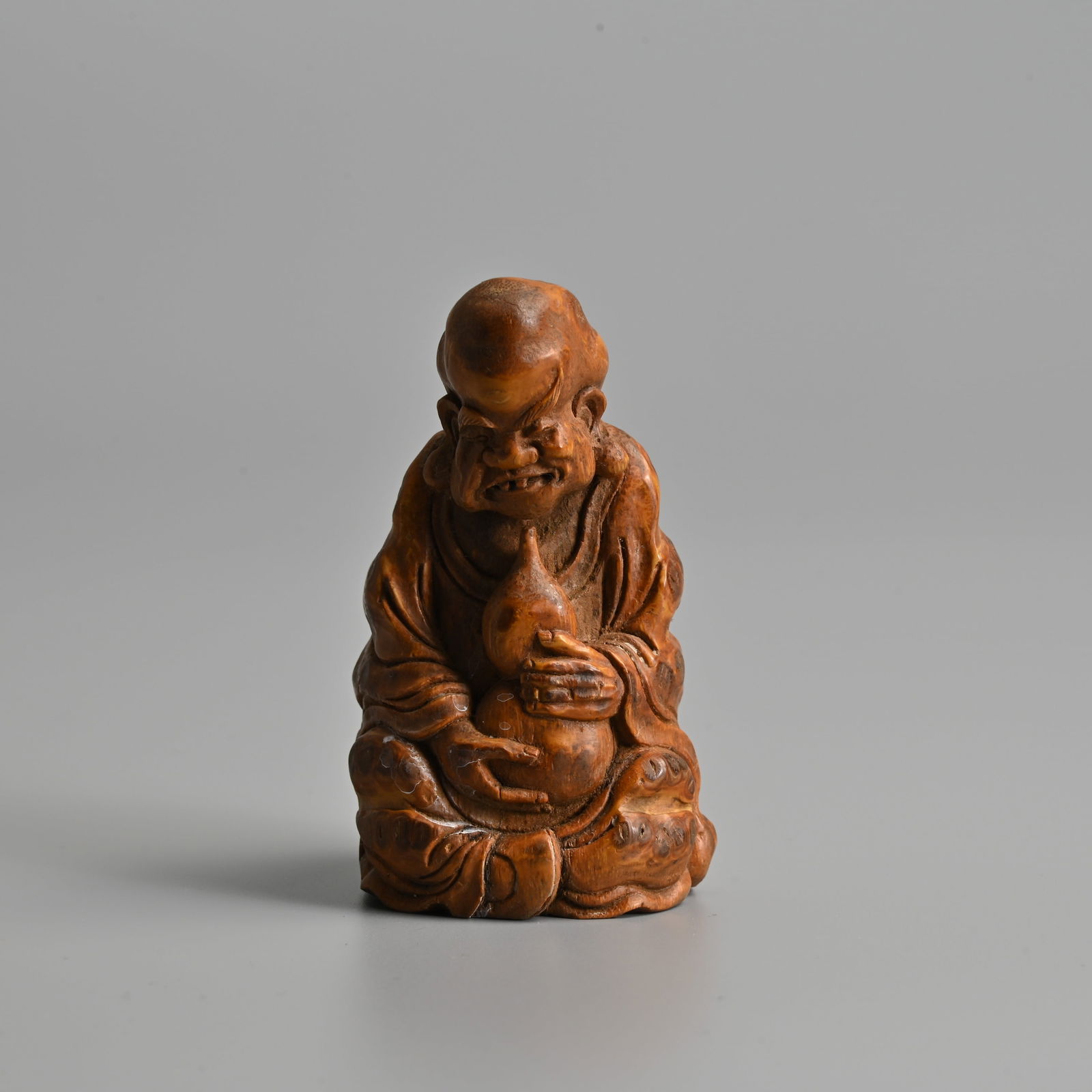 A SMALL CHINESE BAMBOO FIGURE OF AN IMMORTAL, QING DYNASTY.: A SMALL CHINESE BAMBOO FIGURE OF AN IMMORTAL, QING DYNASTY. Seated dressed in robes holding a double gourd bottle. 8.5cm tall. Condition: In good overall condition with no signs of damage or repairs.