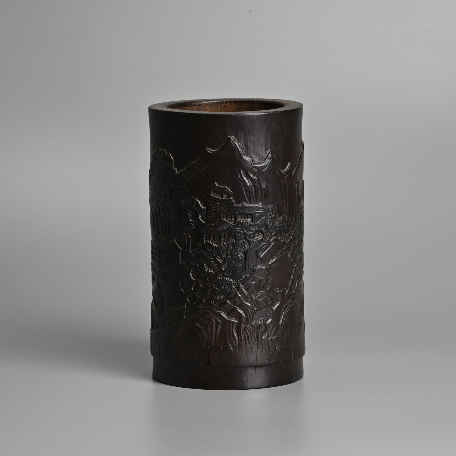 A CHINESE BAMBOO BRUSH POT, BITONG, QING / REPUBLIC PERIOD.: A CHINESE BAMBOO BRUSH POT, BITONG, QING / REPUBLIC PERIOD. Carved in shallow relief with a continuous scene of buildings in a mountainous landscape. 18.3cm tall. Condition: Some fine natural splittin