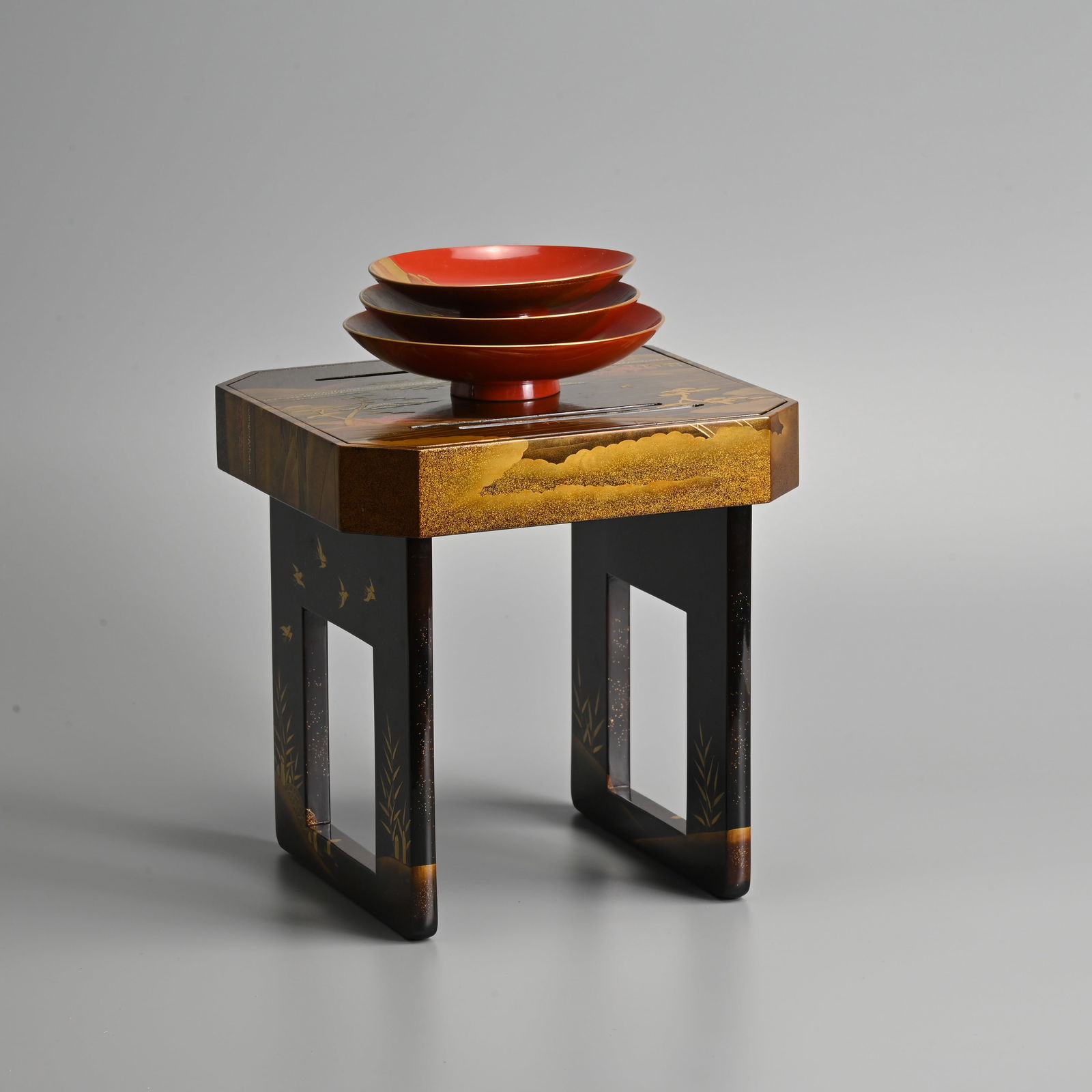 A JAPANESE LACQUER TABLE (KAGETSUDAI) AND SET OF THREE SAKE CUPS BY NAKAMURA SHUNETSU, 20TH CENTURY.: A JAPANESE LACQUER TABLE (KAGETSUDAI) AND SET OF THREE SAKE CUPS BY NAKAMURA SHUNETSU, 20TH CENTURY. The table decorated in black, gold and red lacquer with a farming scene, the red ground cups decora