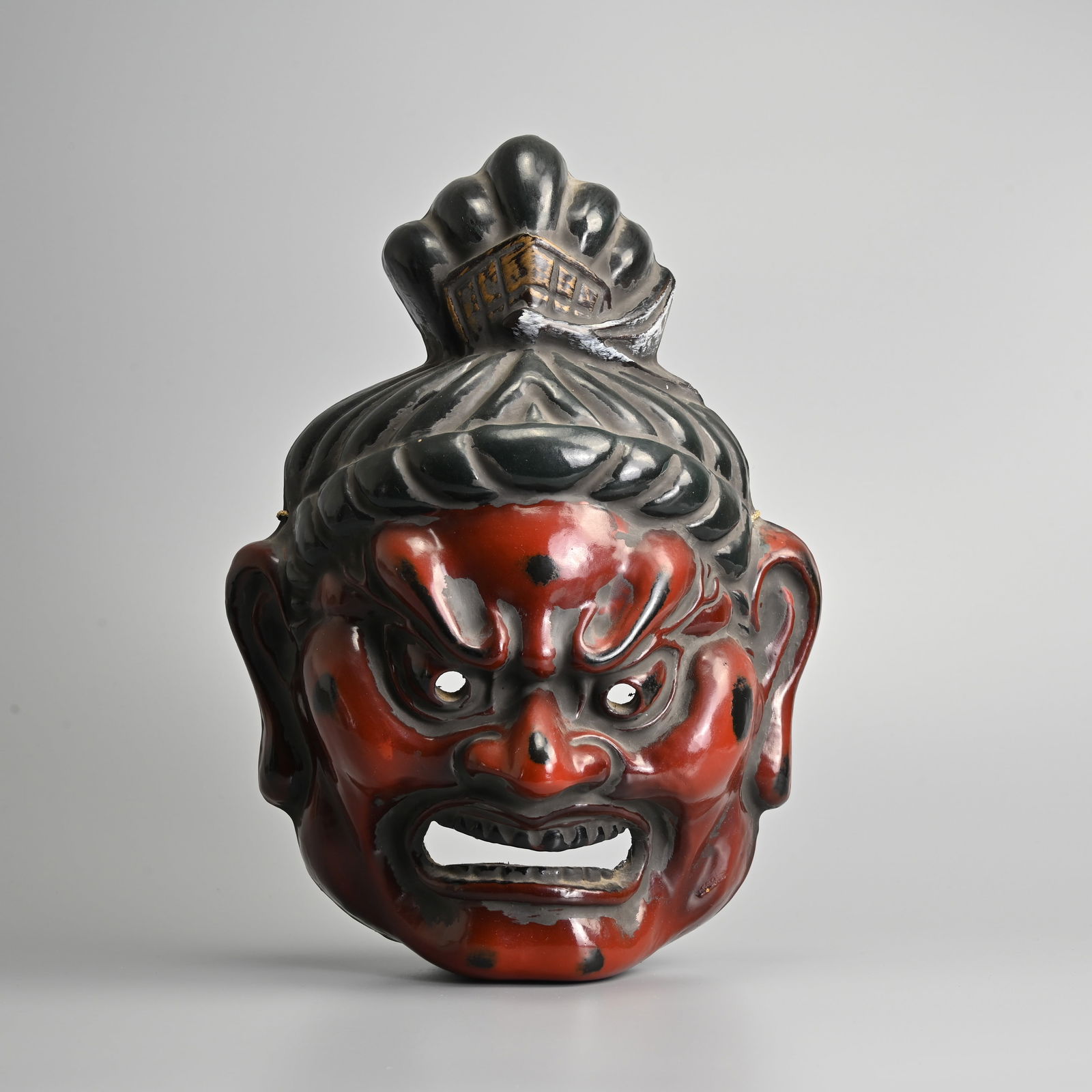 A JAPANESE RED AND BLACK LACQUERED THEATRICAL MASK, 20TH CENTURY.: A JAPANESE RED AND BLACK LACQUERED THEATRICAL MASK, 20TH CENTURY. Depicting a Kongo-rikishi (Nio), a guardian spirit, with apertures for eyes and mouth, applied with signed paper label to reverse, 35
