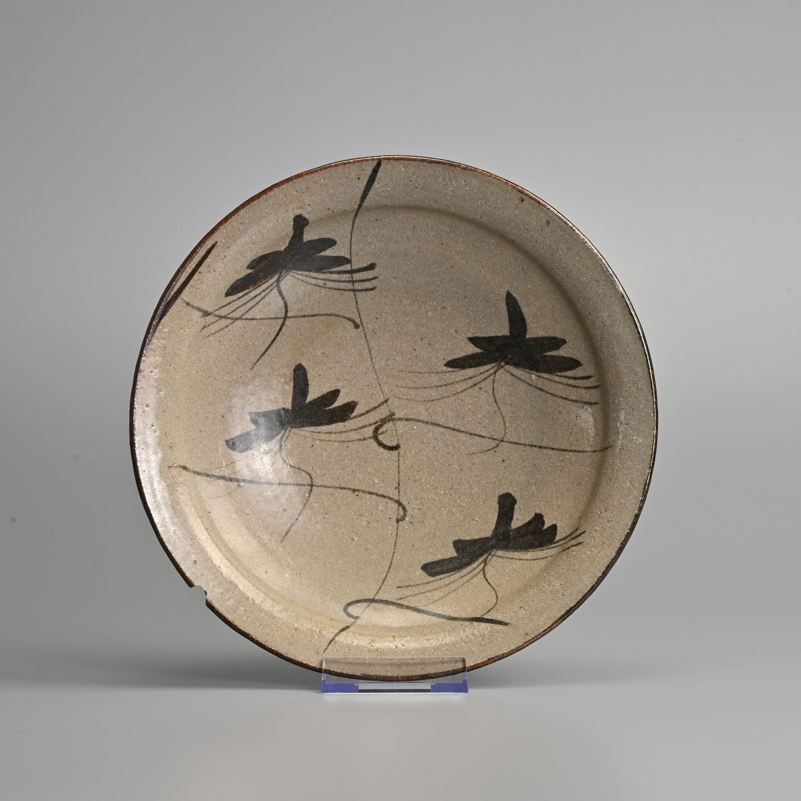 A JAPANESE STONEWARE KARATSU WARE DISH, 20TH CENTURY, IMPRESSED THREE DOT MARK.: A JAPANESE STONEWARE KARATSU WARE DISH, 20TH CENTURY, IMPRESSED THREE DOT MARK. Painted with trailing iron brown leaves, within a brown lined rim, 21.4 cm diam. Condition: Rim chip 1.3 cm wide, otherw