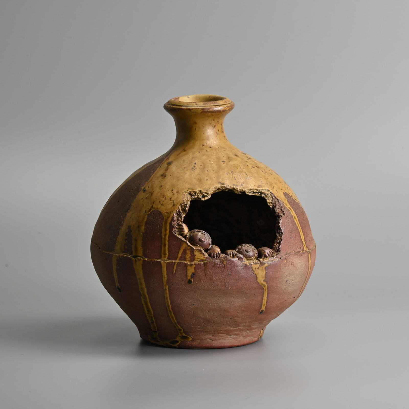 WATO ABE (B. 1937, TOKYO) EARTHENWARE GLOBULAR BOTTLE VASE.: WATO ABE (B. 1937, TOKYO) EARTHENWARE GLOBULAR BOTTLE VASE. Glazed in a streaked pale ochre to neck and shoulders, pierced to the centre and applied with two small figures peering out, glazed to inter