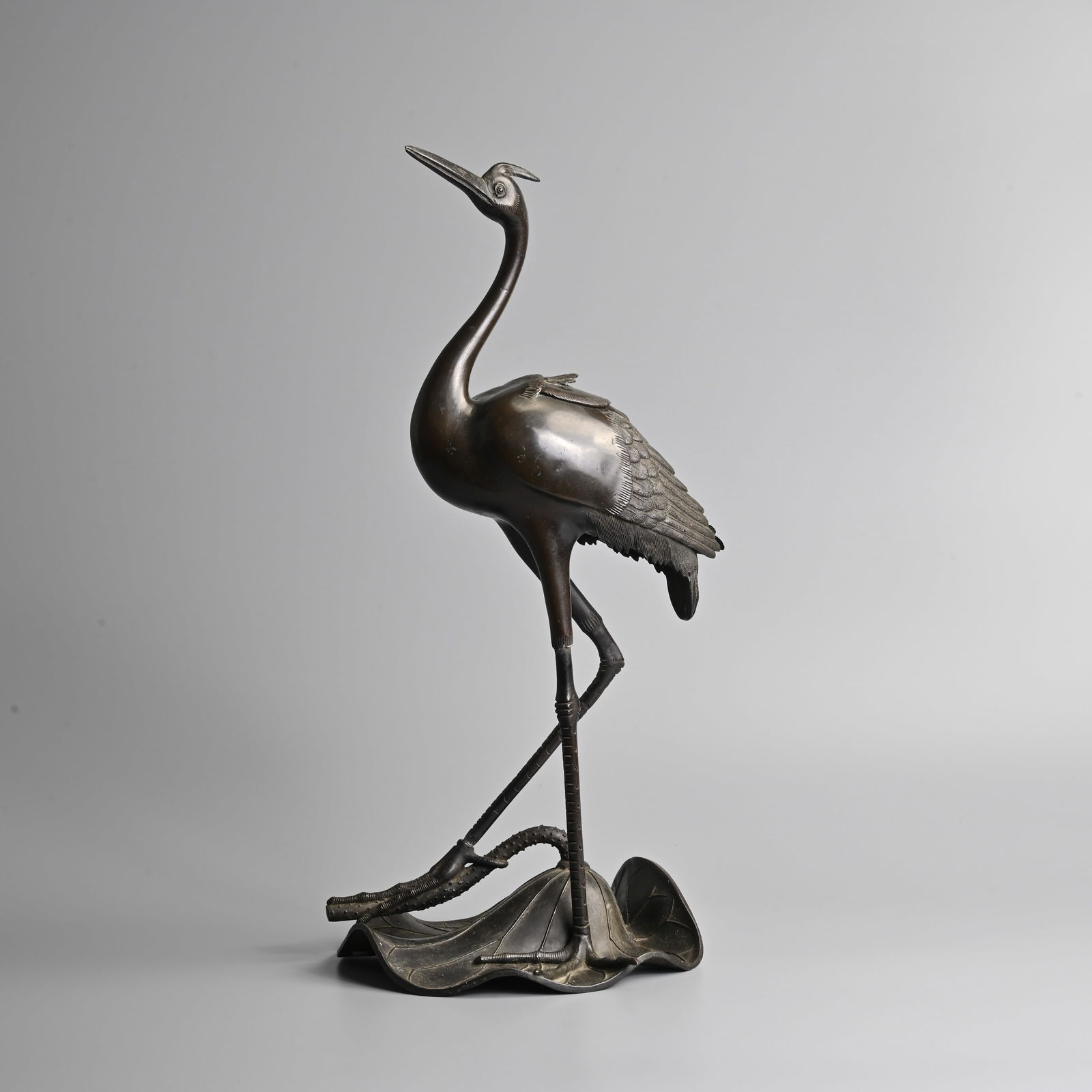 A LARGE JAPANESE BRONZE INCENSE BURNER AND COVER IN THE FORM OF A CRANE, MEIJI PERIOD.: A LARGE JAPANESE BRONZE INCENSE BURNER AND COVER IN THE FORM OF A CRANE, MEIJI PERIOD. Modelled standing on a large lotus leaf with on foot on the stem. Small cover to the back of the bird revealing t