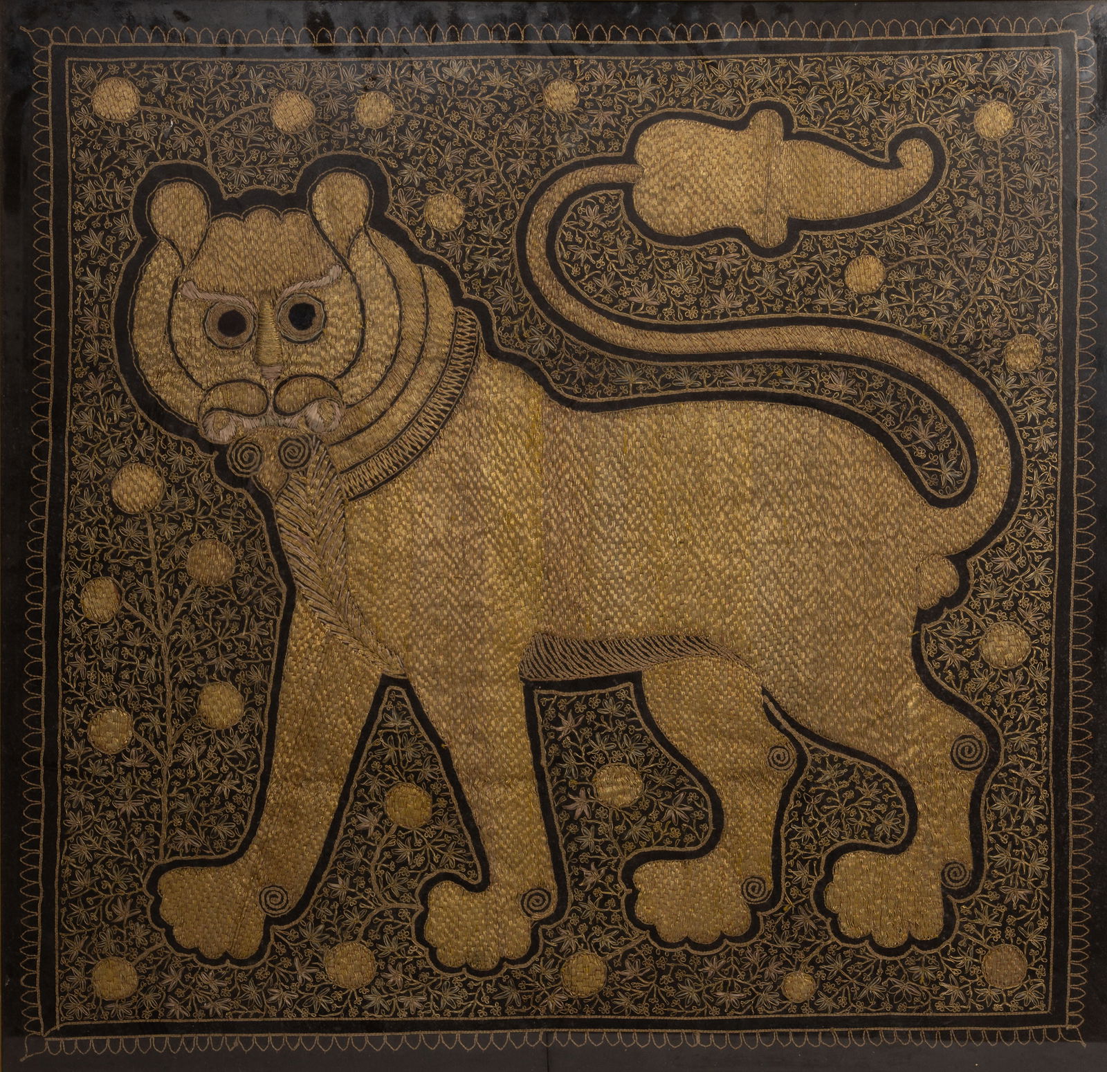 FRAMED MIDDLE EASTERN EMBROIDERED GOLD THREAD PANEL OF A LION, 20TH CENTURY.: FRAMED MIDDLE EASTERN EMBROIDERED GOLD THREAD PANEL OF A LION, 20TH CENTURY. Finely embroidered with a bold lion rampant, standing four square with tail upright, on a dense foliate pattern black groun