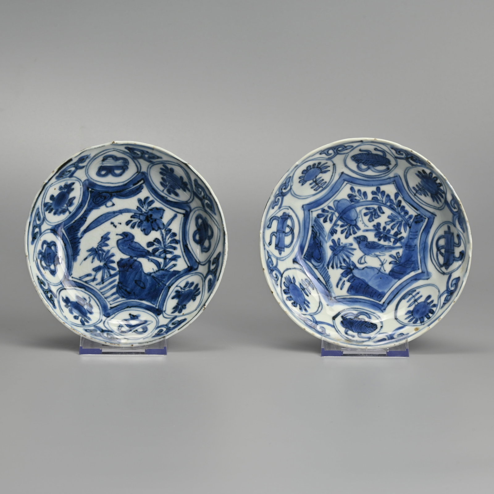 A MATCHED PAIR OF CHINESE PORCELAIN BLUE AND WHITE SAUCERS, LATE MING DYNASTY, WANLI PERIOD: Each painted with a bird perched on rockwork before peony in landscape, the border with scrolls, flowers and fans within circular swagged cartouches, the undersides with foliate panels, approx.. 14 cm