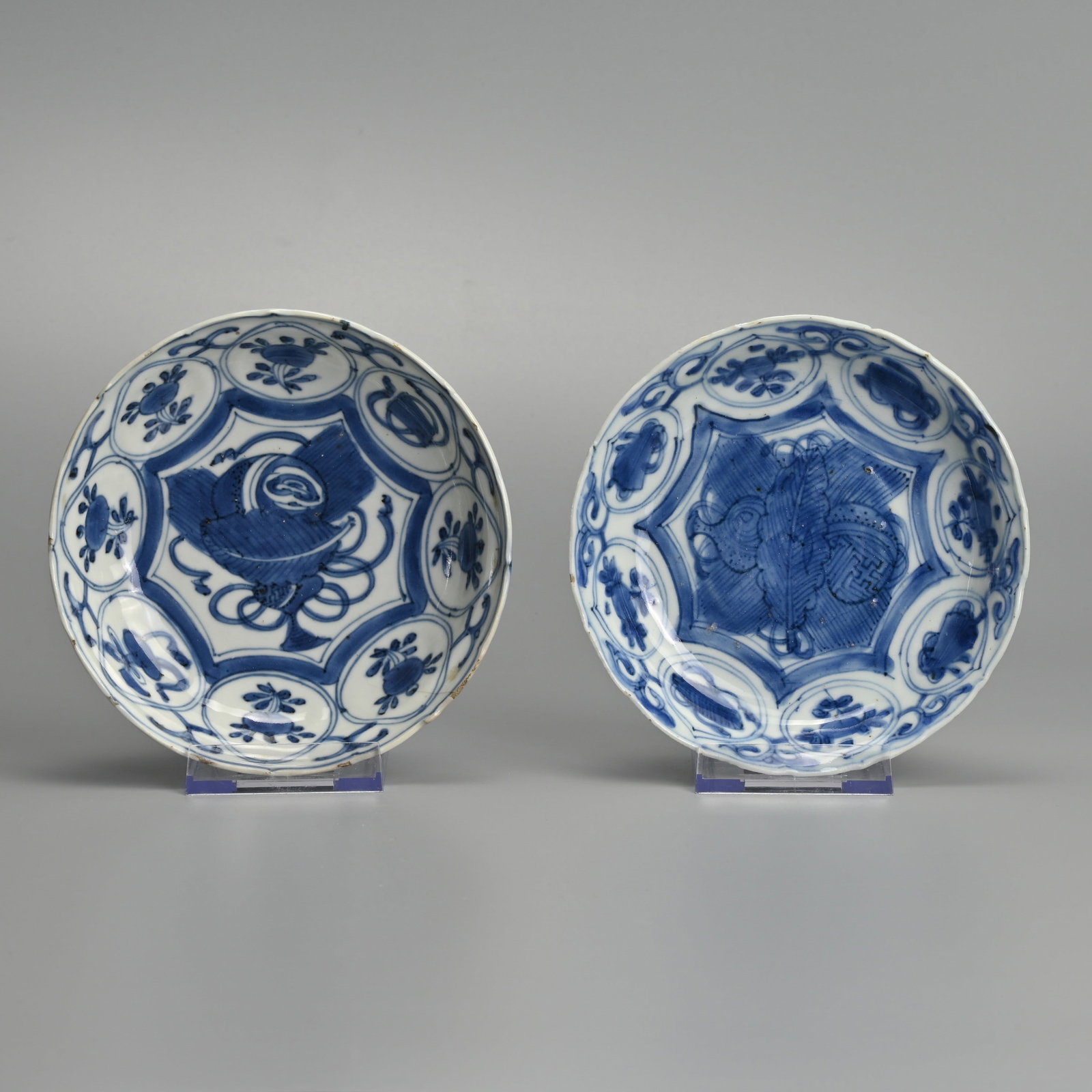 TWO CHINESE KRAAK PORCELAIN BLUE AND WHITE SAUCERS, LATE MING DYNASTY, WANLI PERIOD (1573-1619).: Each painted with a ball, leaves and scrollwork within a star shaped cartouche, the border with scrolls and flowers within circular cartouches, the undersides with foliate panels, approx. 14 cm diam. 