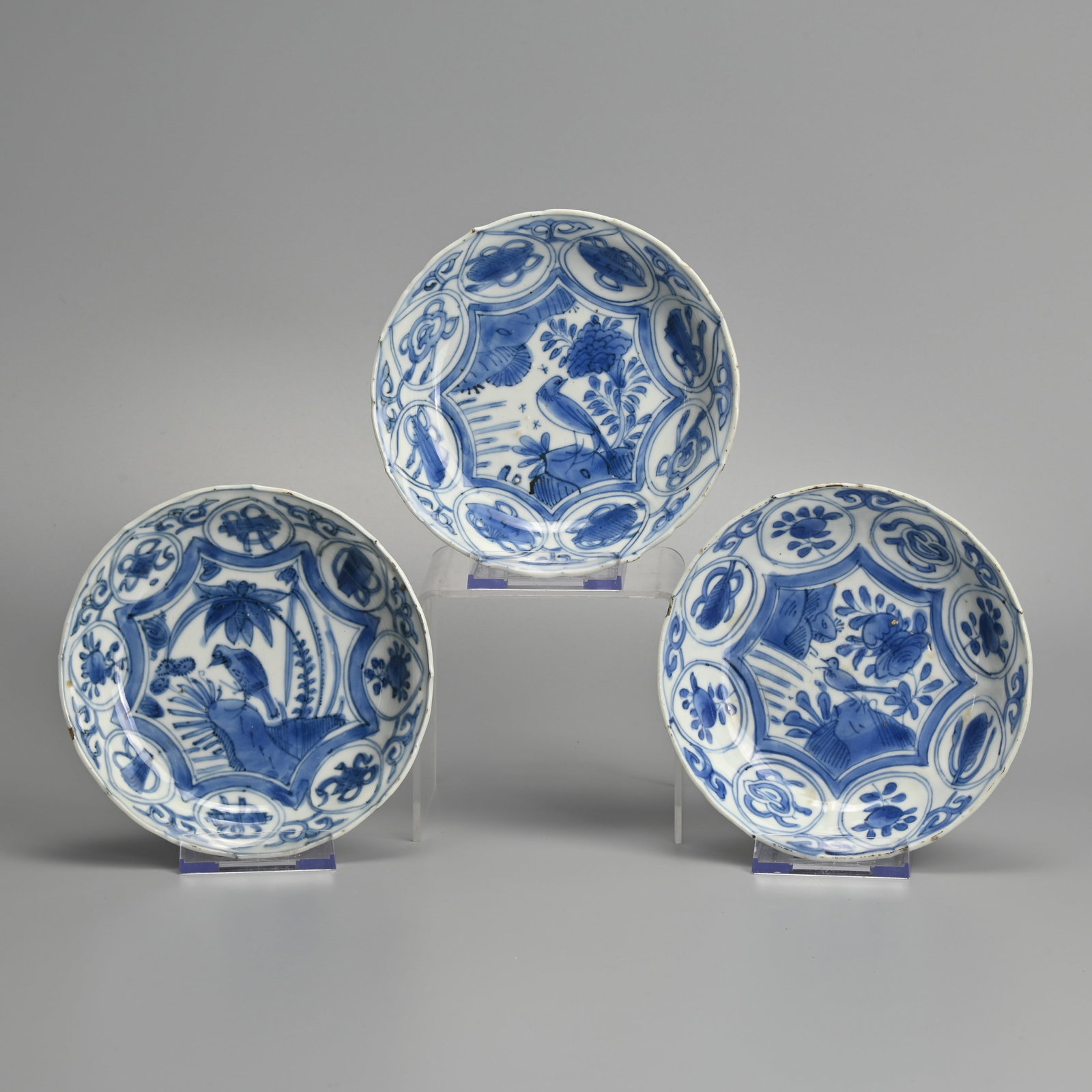 A MATCHED SET OF THREE CHINESE PORCELAIN BLUE AND WHITE SAUCERS, LATE MING DYNASTY, WANLI PERIOD: Each painted with a bird perched on rockwork before peony in landscape, the border with scrolls, flowers and fans within circular swagged cartouches, the undersides with foliate panels, approx.. 14 cm