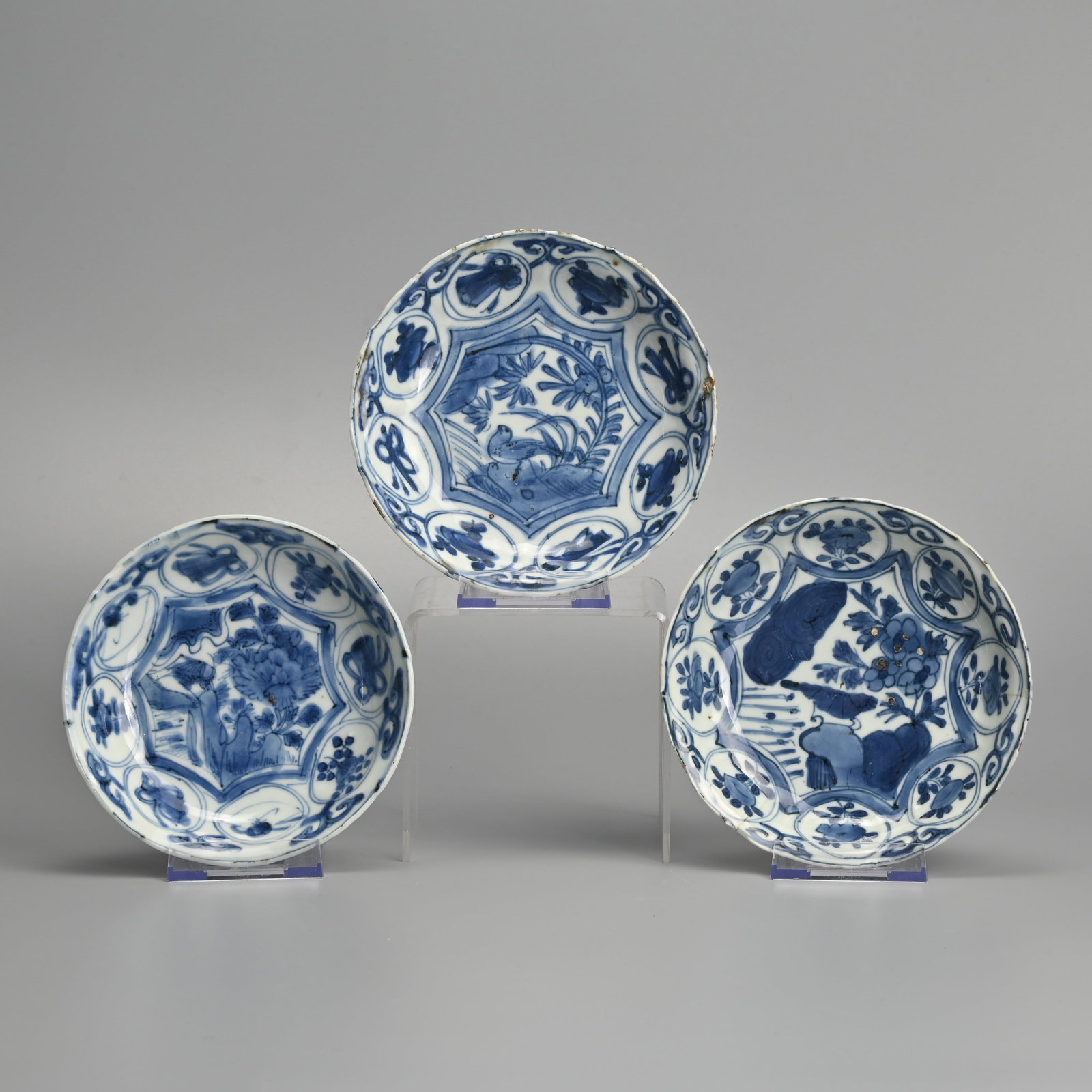A MATCHED SET OF THREE CHINESE PORCELAIN BLUE AND WHITE SAUCERS, LATE MING DYNASTY, WANLI PERIOD: Each painted with a bird perched on rockwork before peony in landscape, the border with scrolls, flowers and fans within circular swagged cartouches, the undersides with foliate panels, approx.. 14 cm