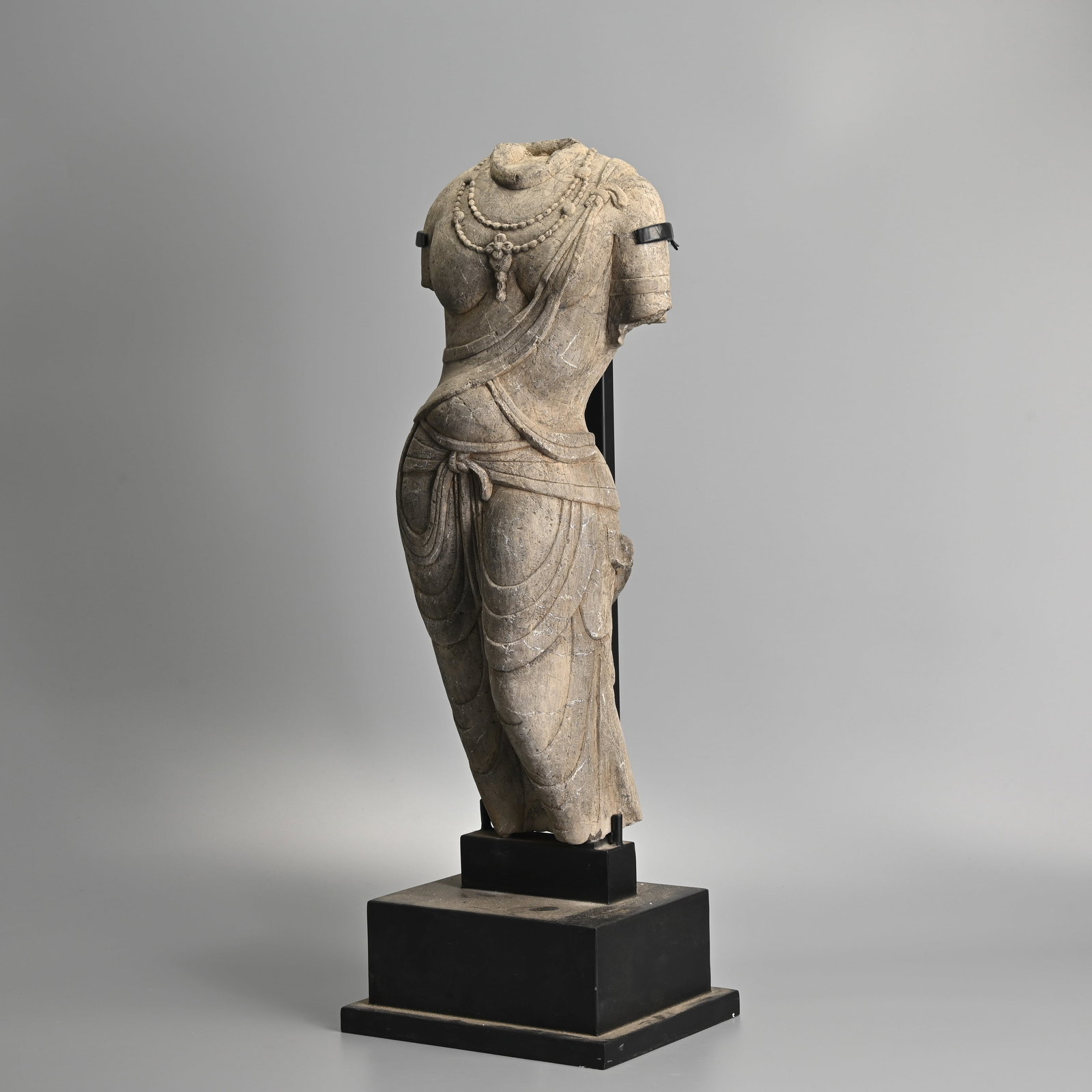 A LARGE CHINESE GREY STONE TORSO OF BODHISATTVA.: Cared in the round, standing in tribhanga pose wearing a necklace with pendant and floral medallions, with the left leg bent at the knee, dressed in a dhoti tied at the left shoulder and at the waist.