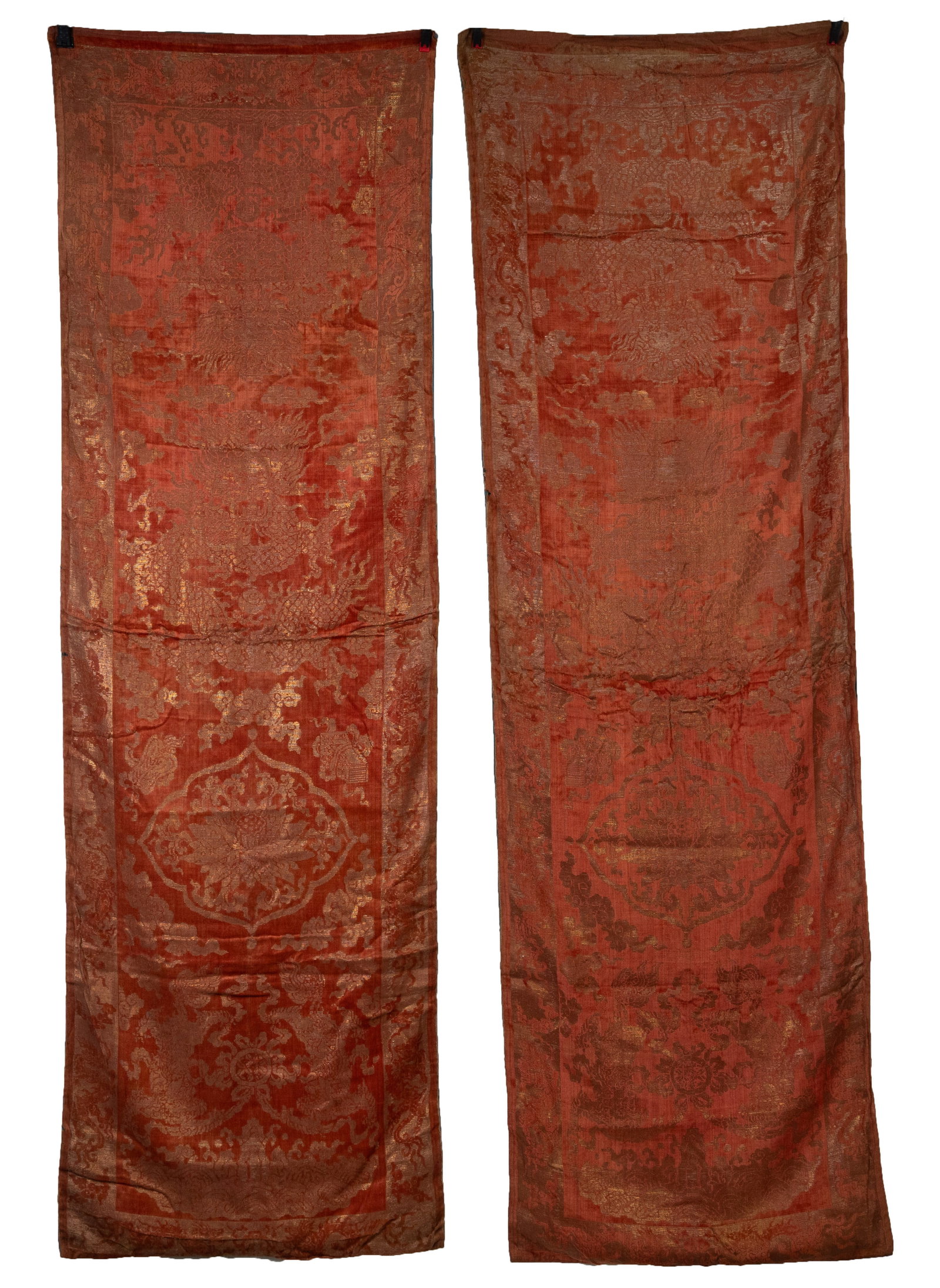 A PAIR OF CHINESE EMBROIDERED SILK CORAL GROUND AND GOLD THREAD 'DRAGON' PANELS, QING DYNASTY,: The coral ground velvet silk woven with lotus flowers, precious objects, ruyi shaped clouds before four clawed dragons chasing flaming pearls, within a dragon and cloud pattern border, backed in blue 