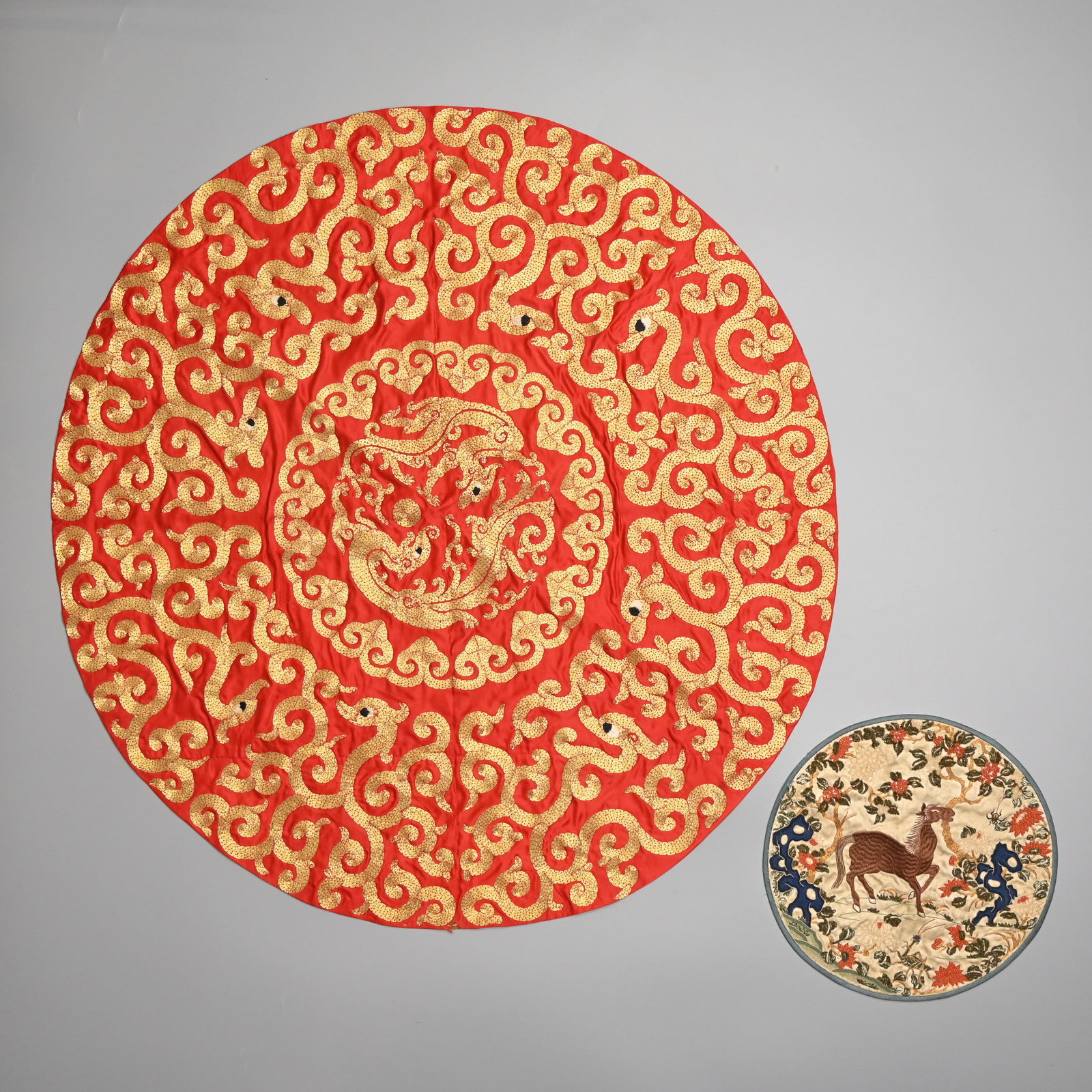 TWO CHINESE EMBROIDERED SILK PANELS, LATE QING DYNASTY AND 20TH CENTURY.: Comprising: a Chinese late Qing Dynasty, embroidered silk circular panel with a horse, a grasshopper & spider in rockwork landscape, applied with coral beadwork flowers and worked with gold thread tre