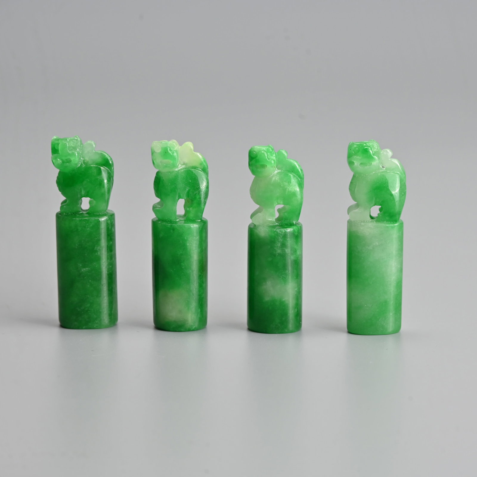 FOUR CHINESE CARVED JADEITE SEAL PENDANTS, 20TH CENTURY.: Of oval and circular forms each surmounted by Dogs of Fo standing foursquare with their head turned to the left. Of good green colour. Approx. 5cm tall. Gross weight 71.5 grams. (4).