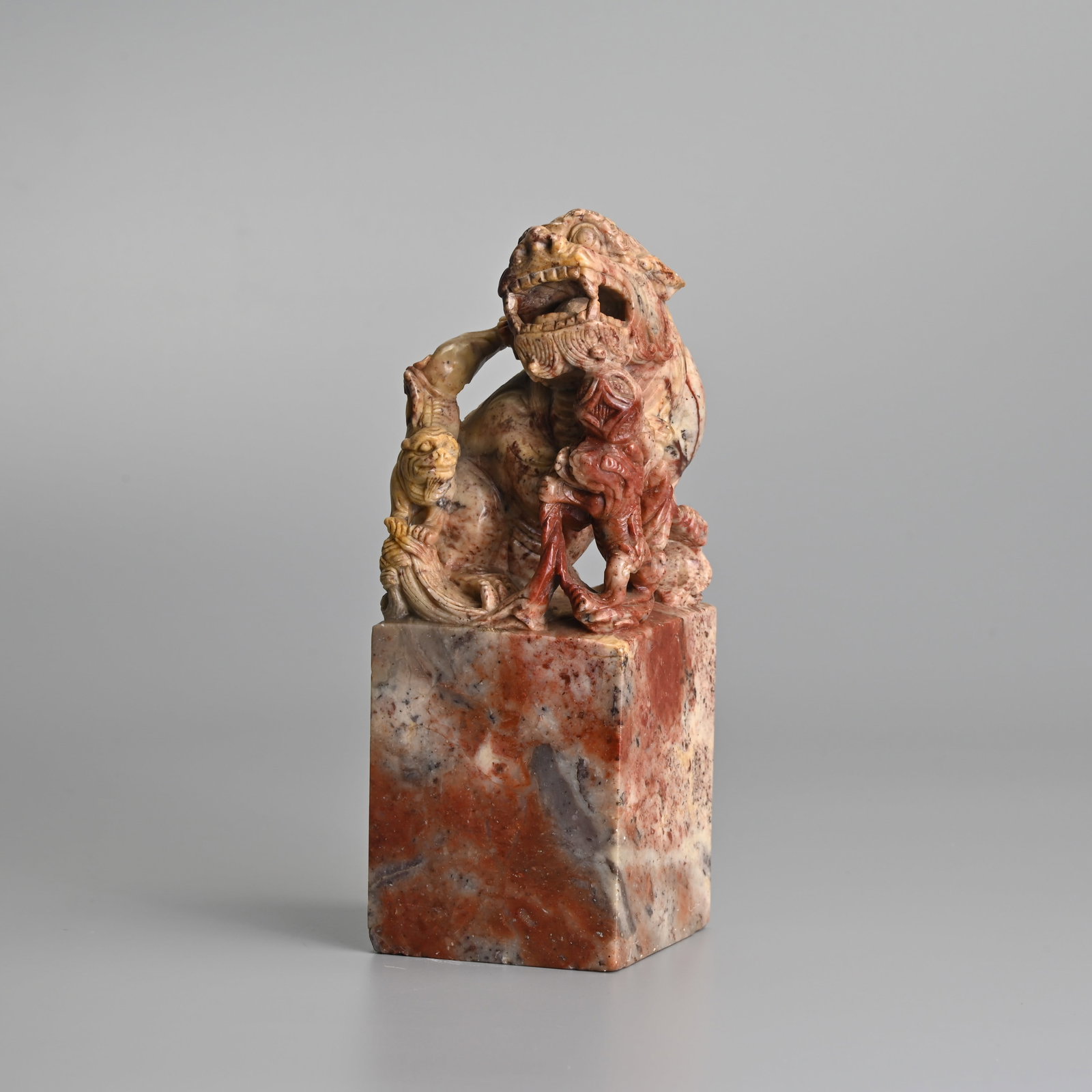 A LARGE CHINESE CARVED SOAPSTONE SEAL, 19/20TH CENTURY.: Featuring a guardian lion with a pearl in its mouth with cubs and a ribboned brocade ball. 18cm tall, square base 6.5cm x 6.5cm.